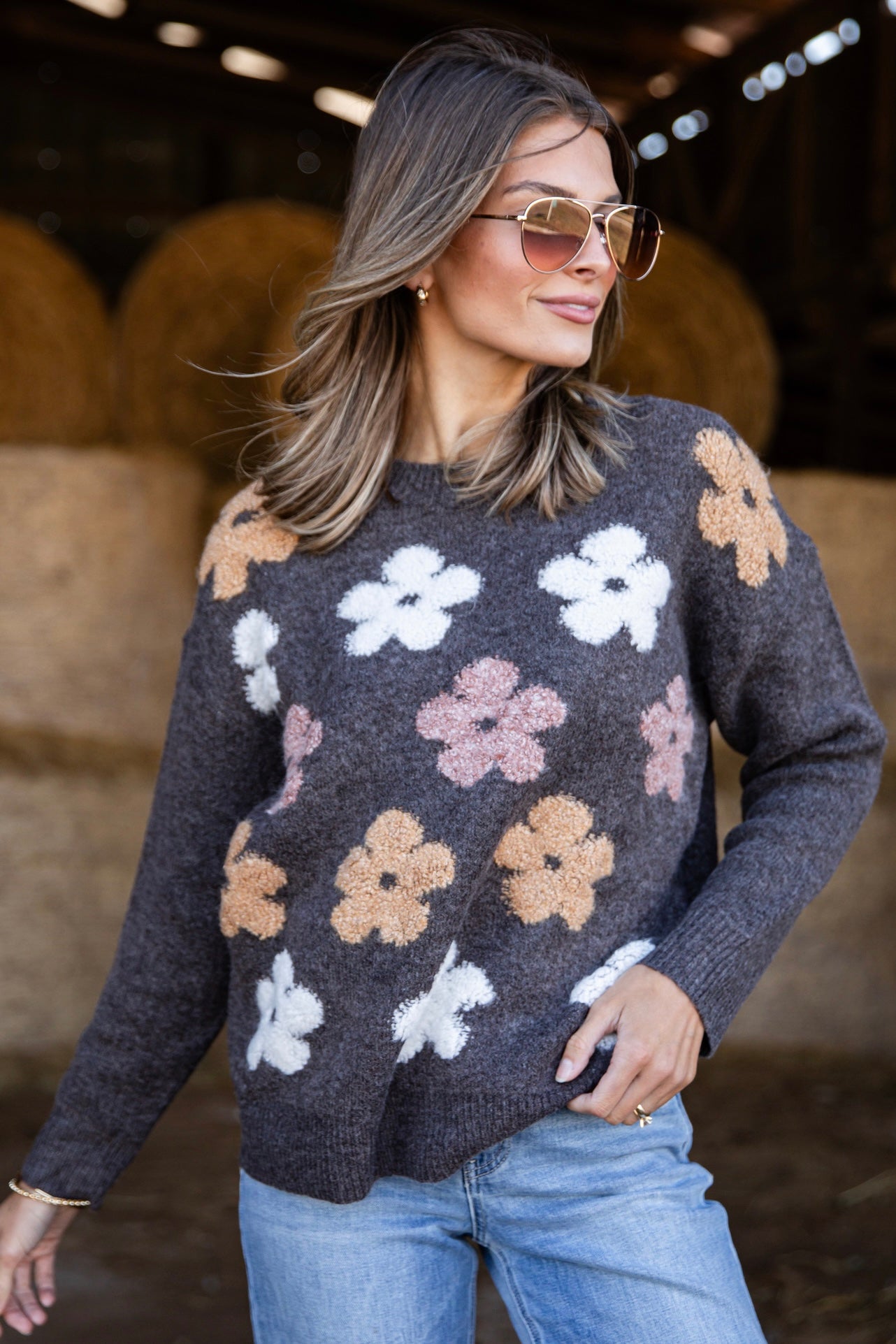 Woman wearing a floral sweater in an indoor setting with hay bales in the background