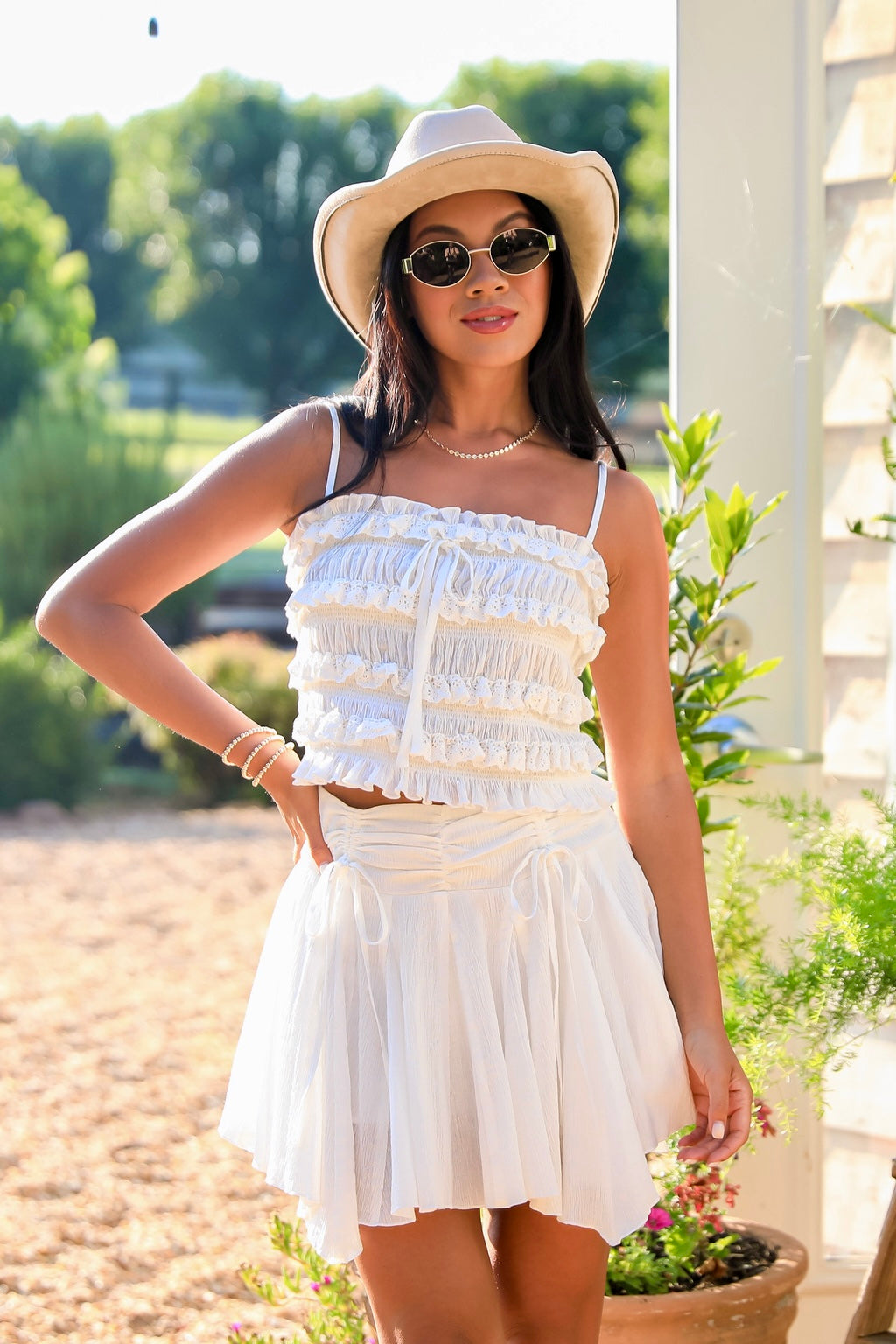 Woman in a white outfit with a hat and sunglasses standing outdoors.