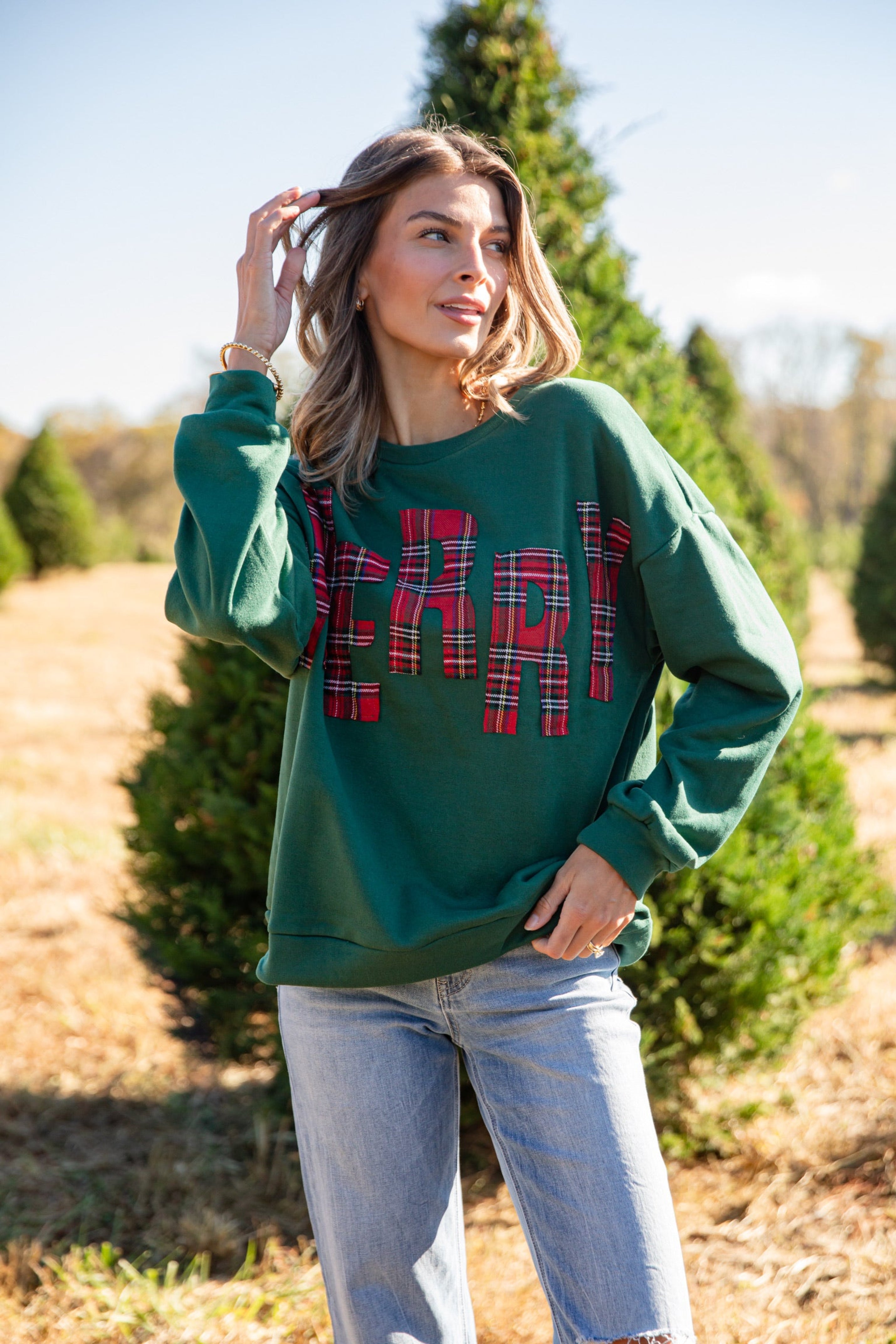 Woman wearing a green sweatshirt with plaid lettering in a Christmas tree lot