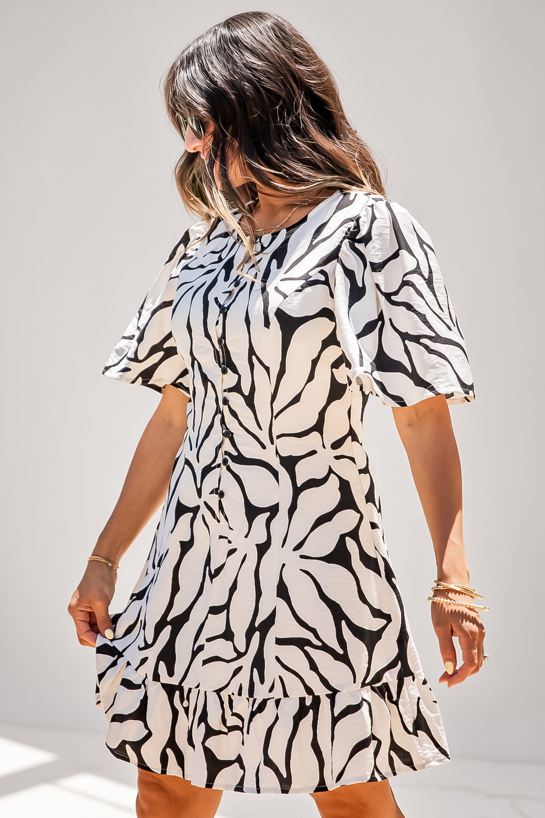 A woman wearing a short-sleeve dress with a bold black and off-white abstract leaf pattern, photographed against a plain light gray studio background.