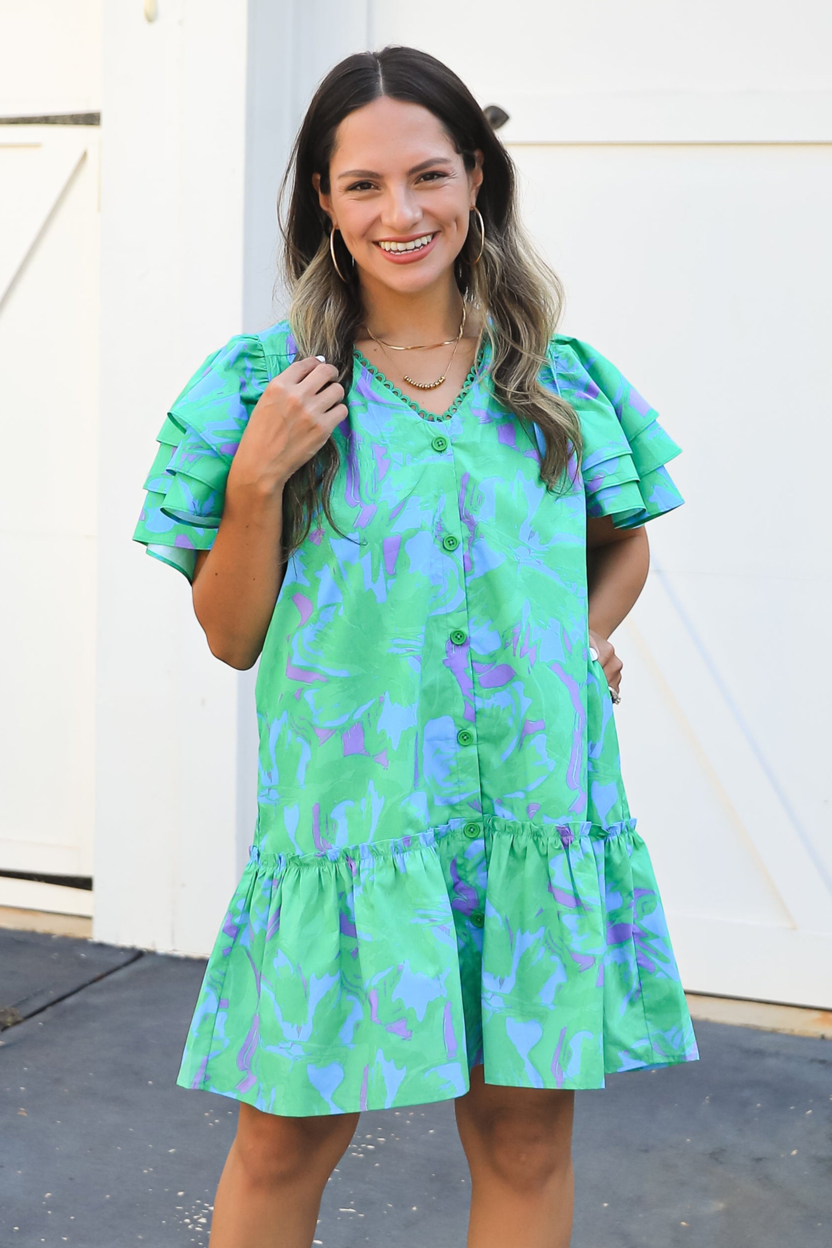 Woman wearing a green floral dress and white boots standing in front of a white door.