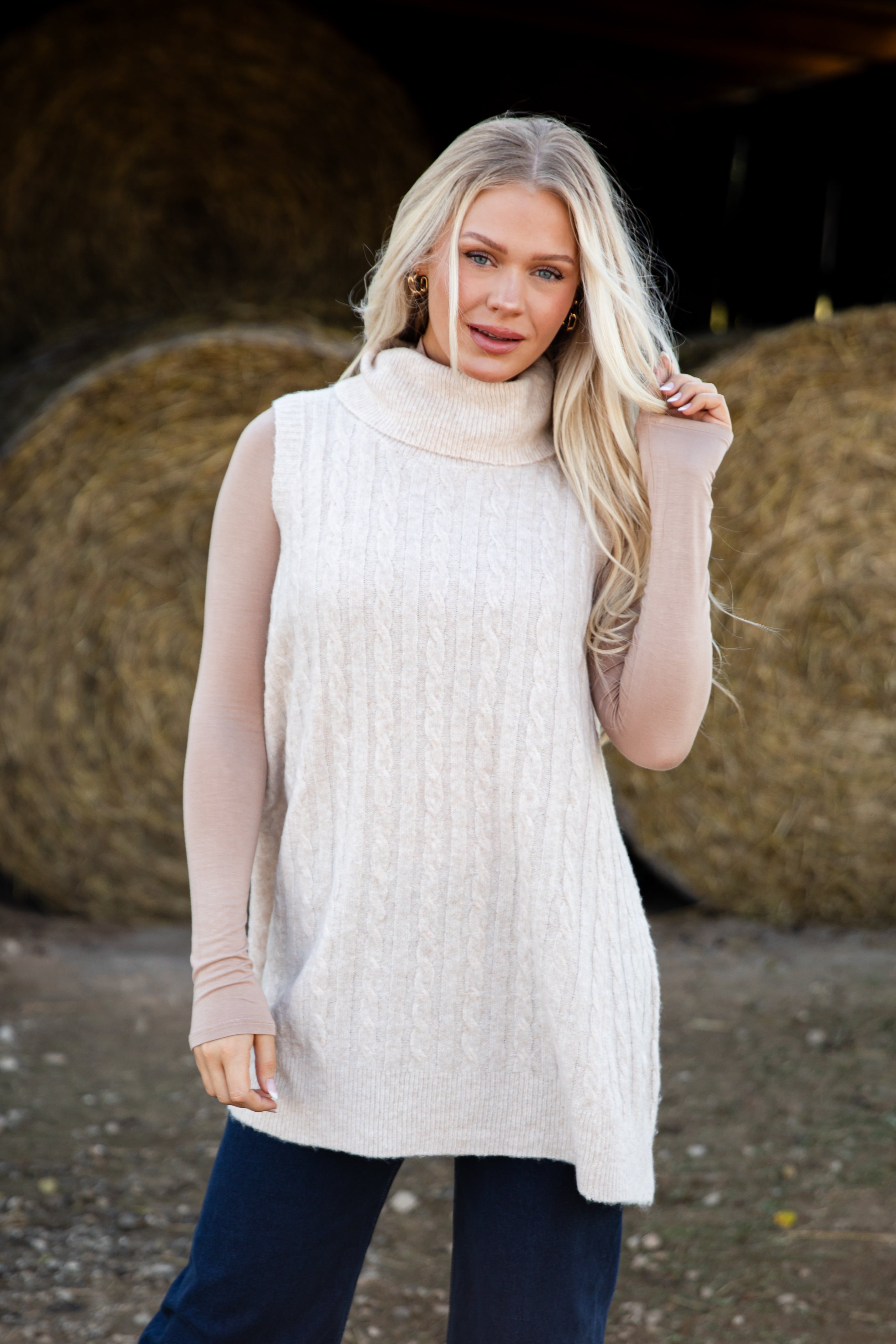Woman wearing a cream-colored sleeveless sweater with bales of hay in the background