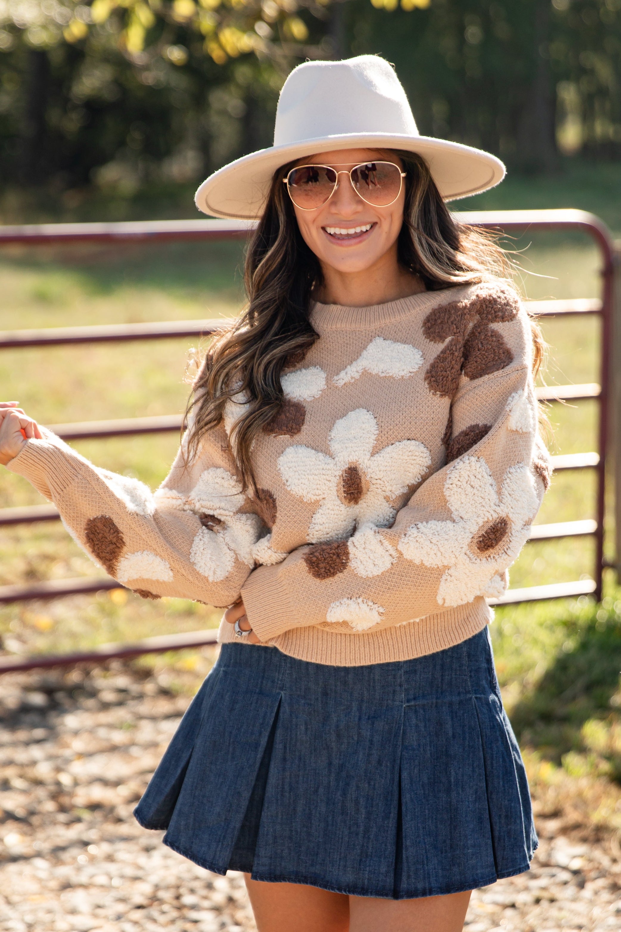 Woman wearing a floral sweater, denim skirt, and beige boots outdoors.