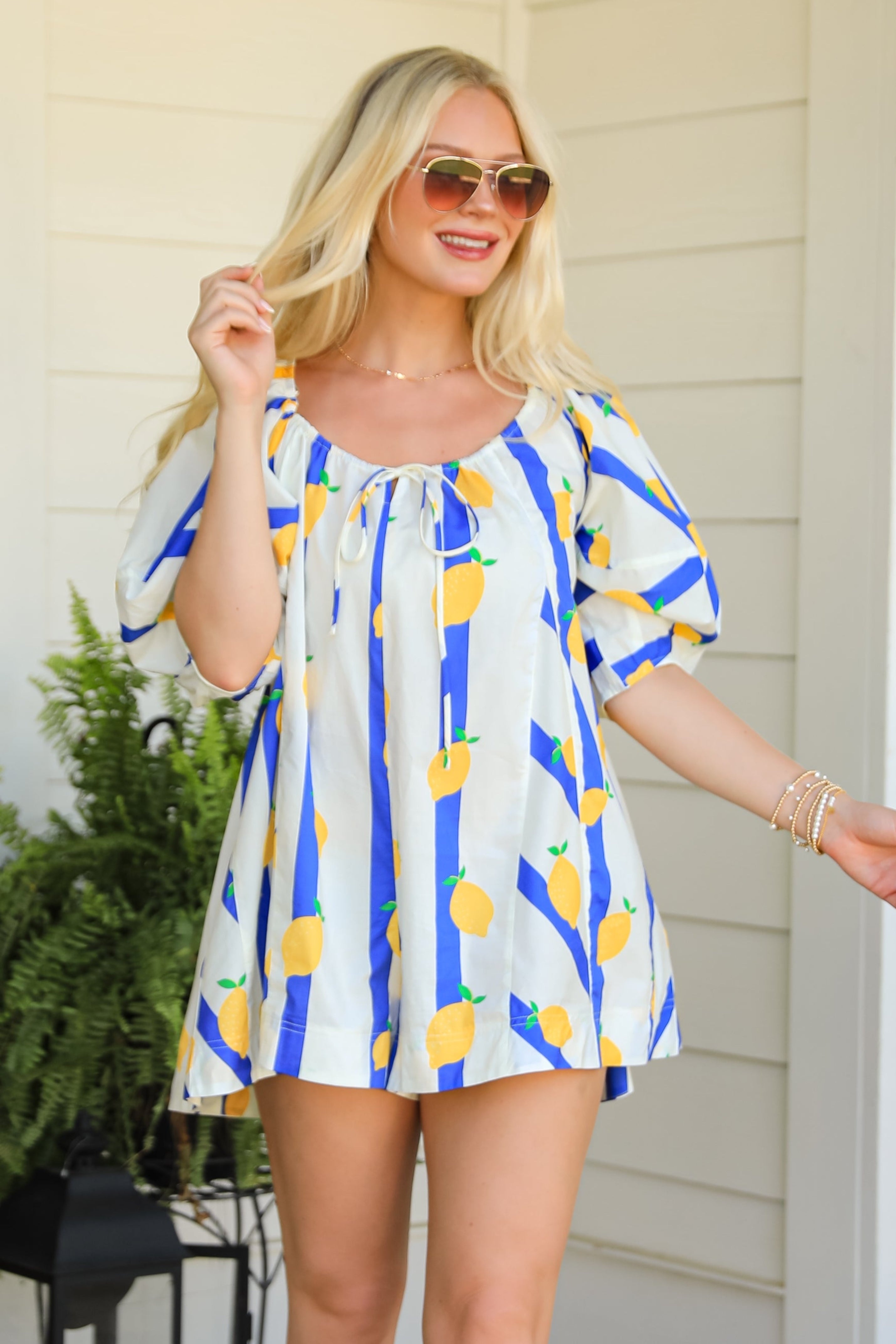 Woman in a colorful dress and white boots standing on a patio with plants and a lantern.