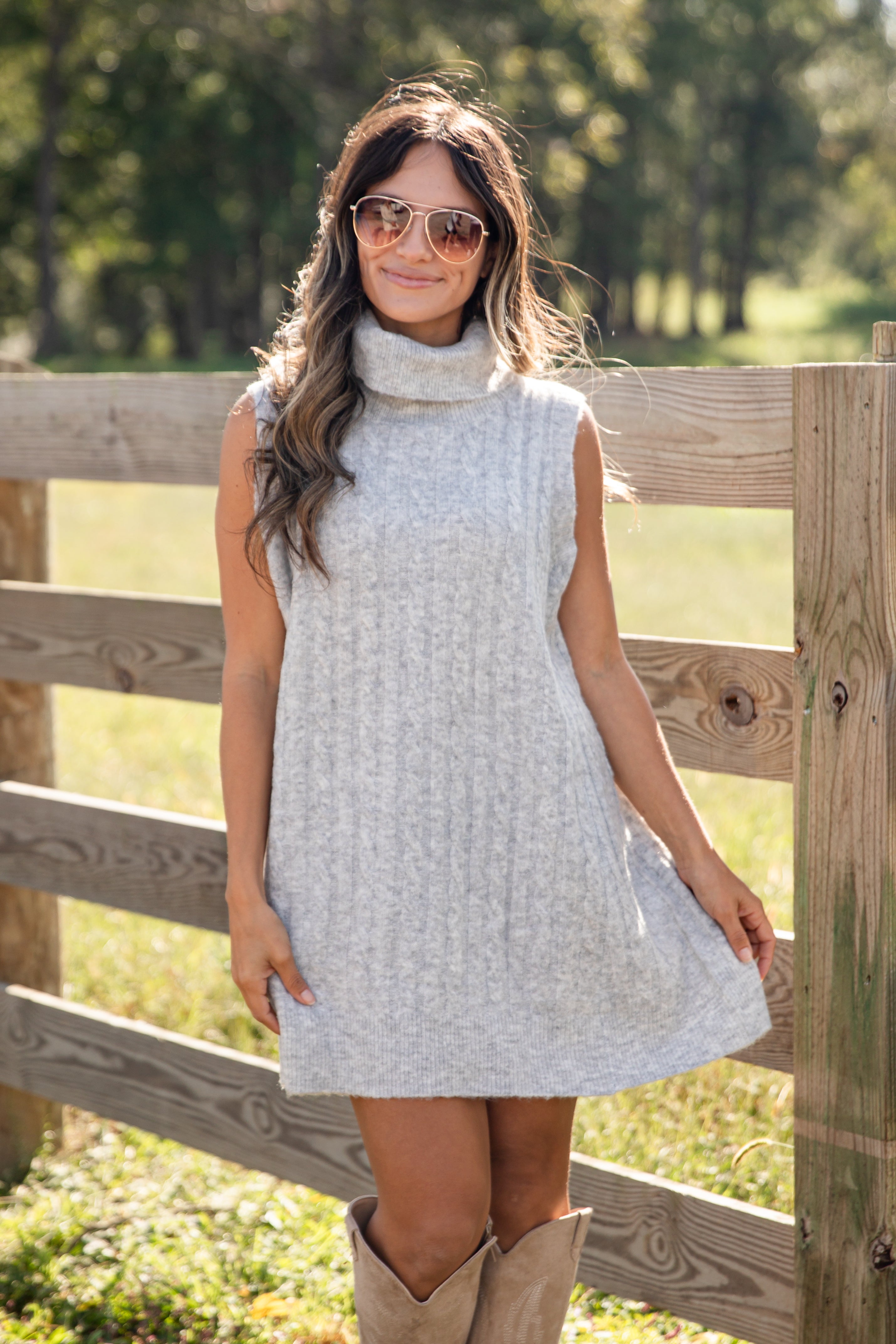 Woman wearing a light gray sleeveless dress with a turtleneck in a natural setting.