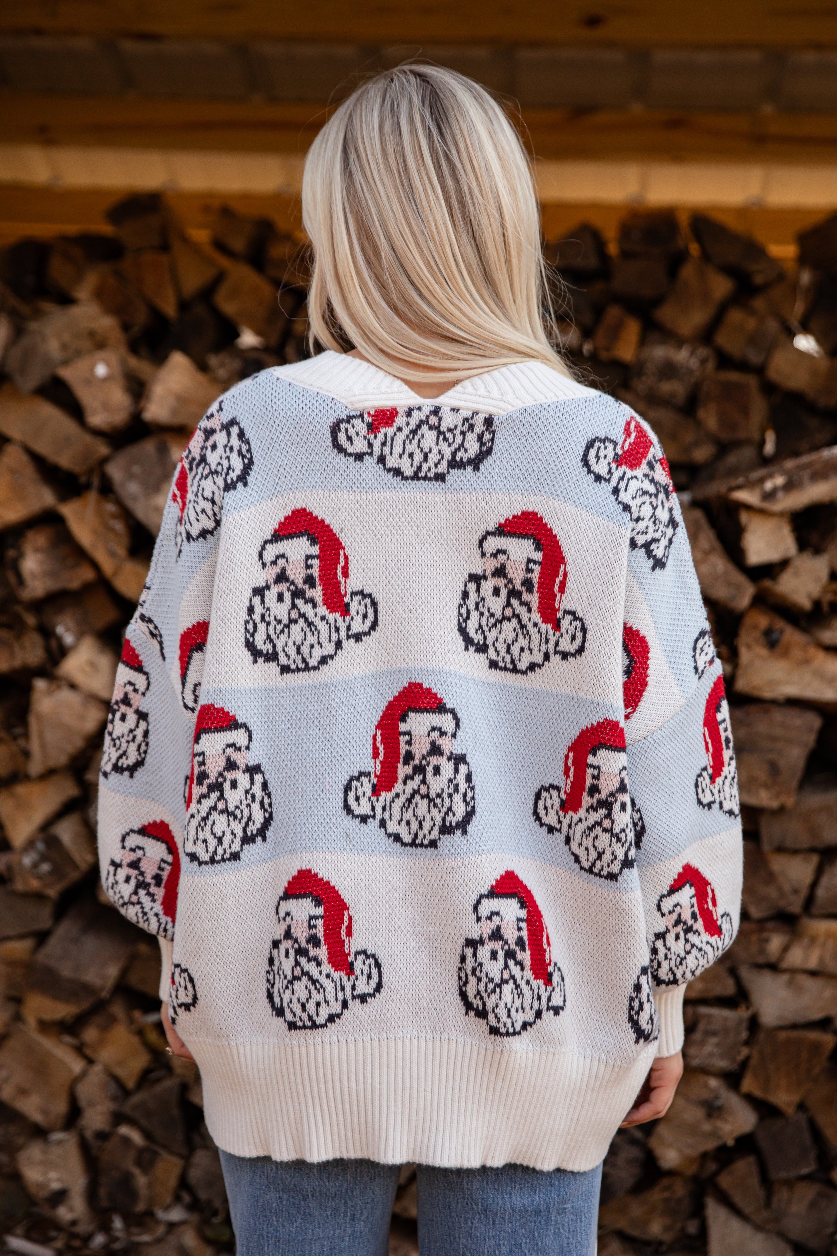 Person wearing a sweater with Santa Claus patterns standing in front of stacked firewood.