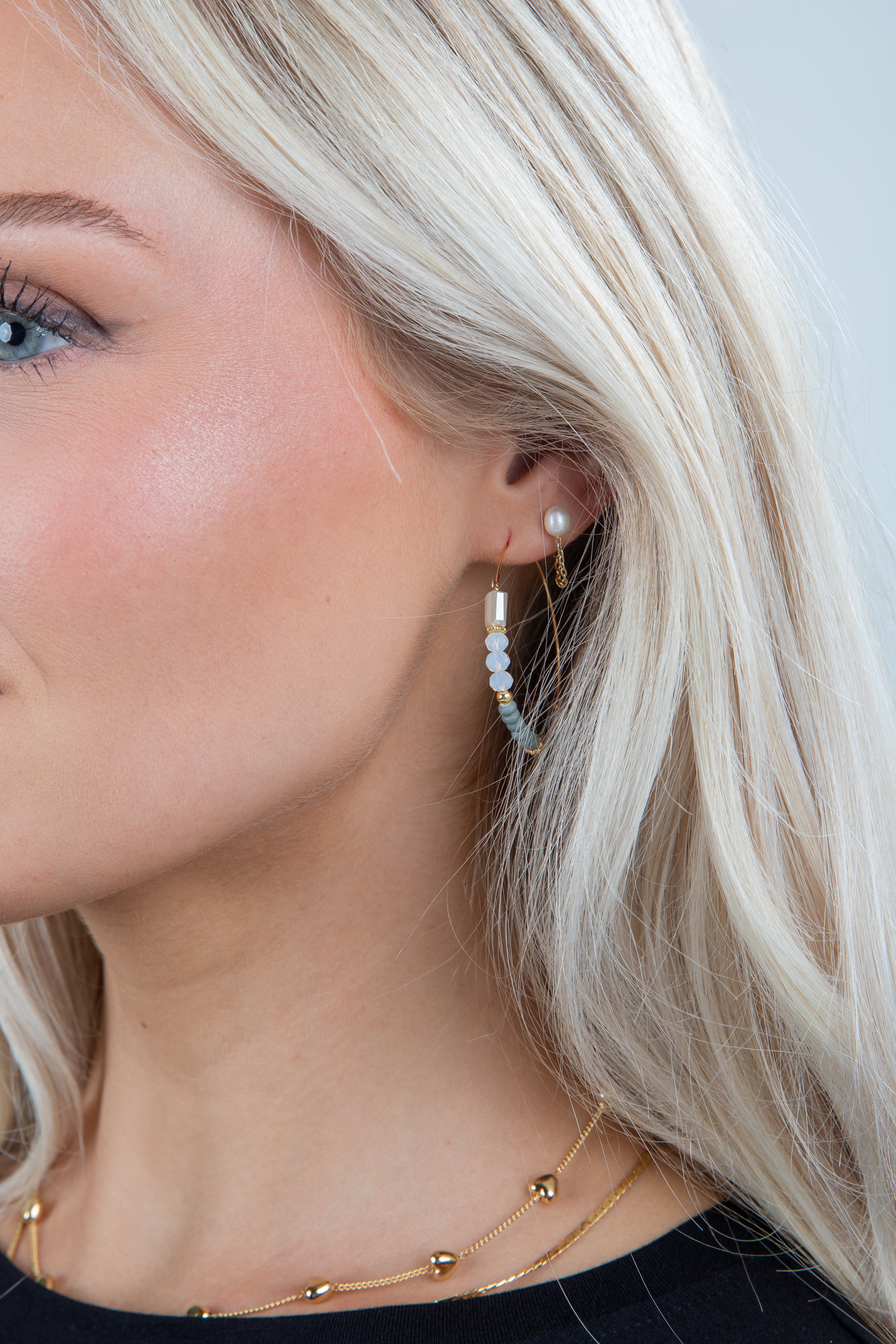 Close-up of a person wearing pearl hoop earrings with a neutral background
