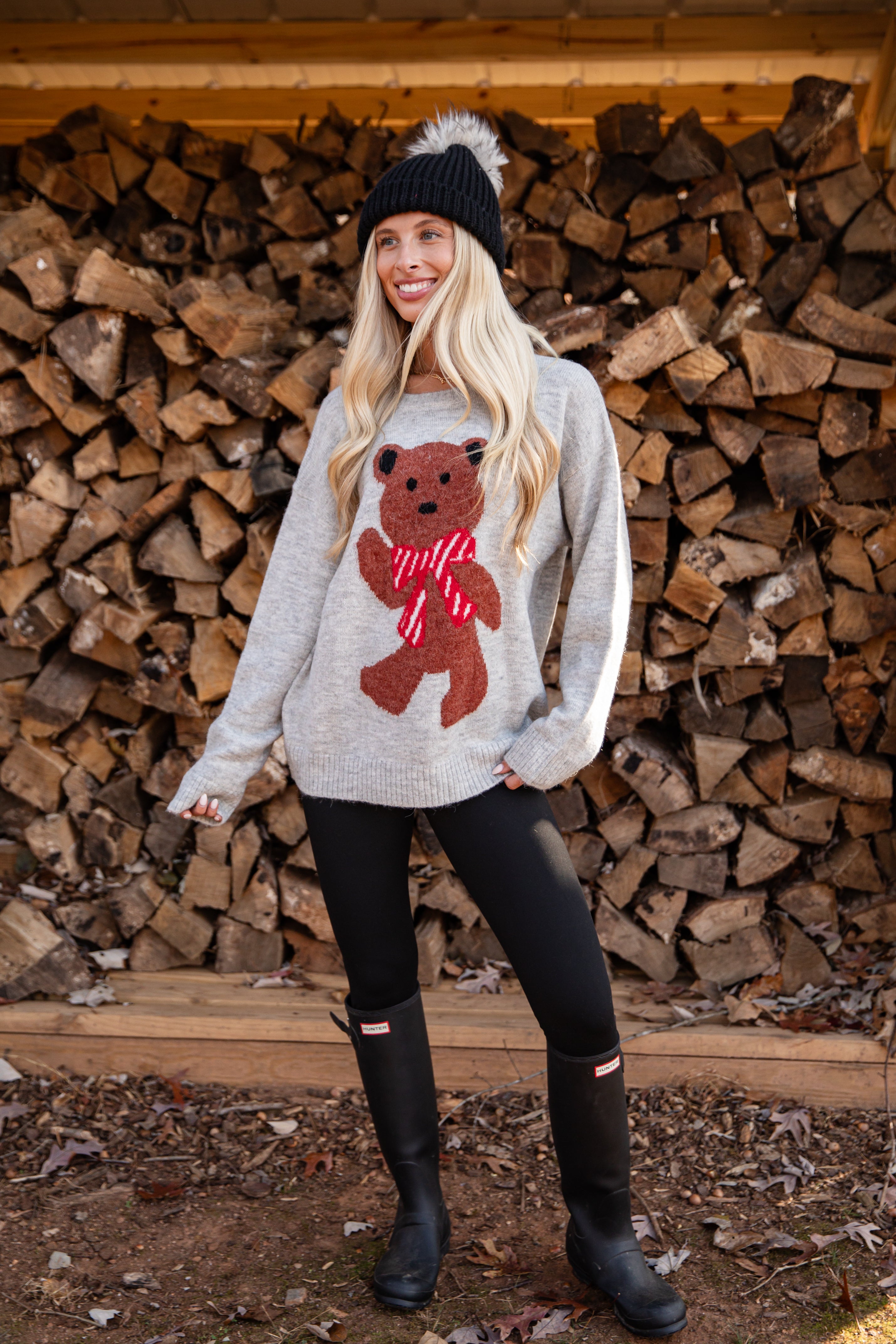 Woman wearing a sweater with a bear design in front of stacked firewood.