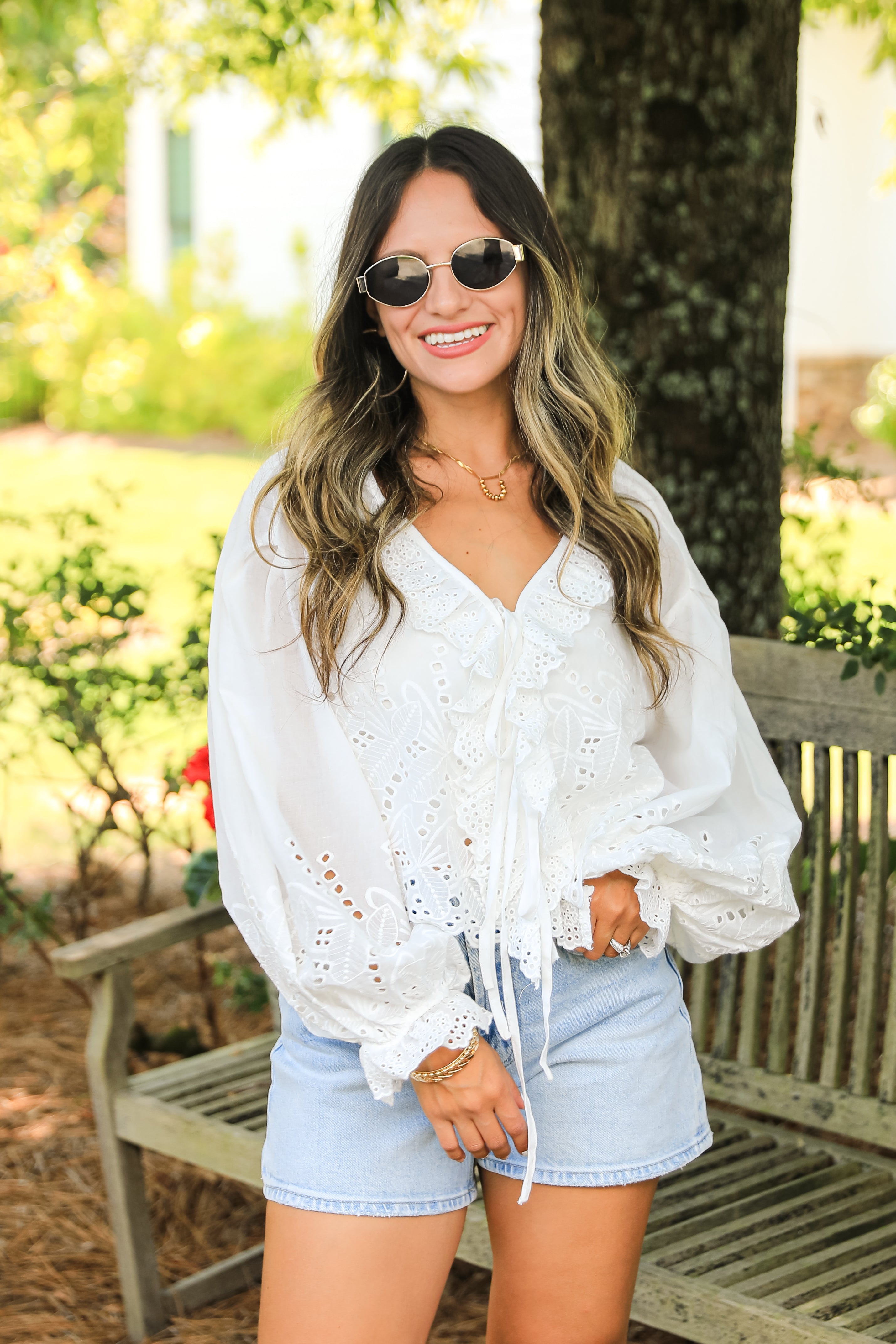 Woman wearing a white blouse with eyelet details and denim shorts outdoors.