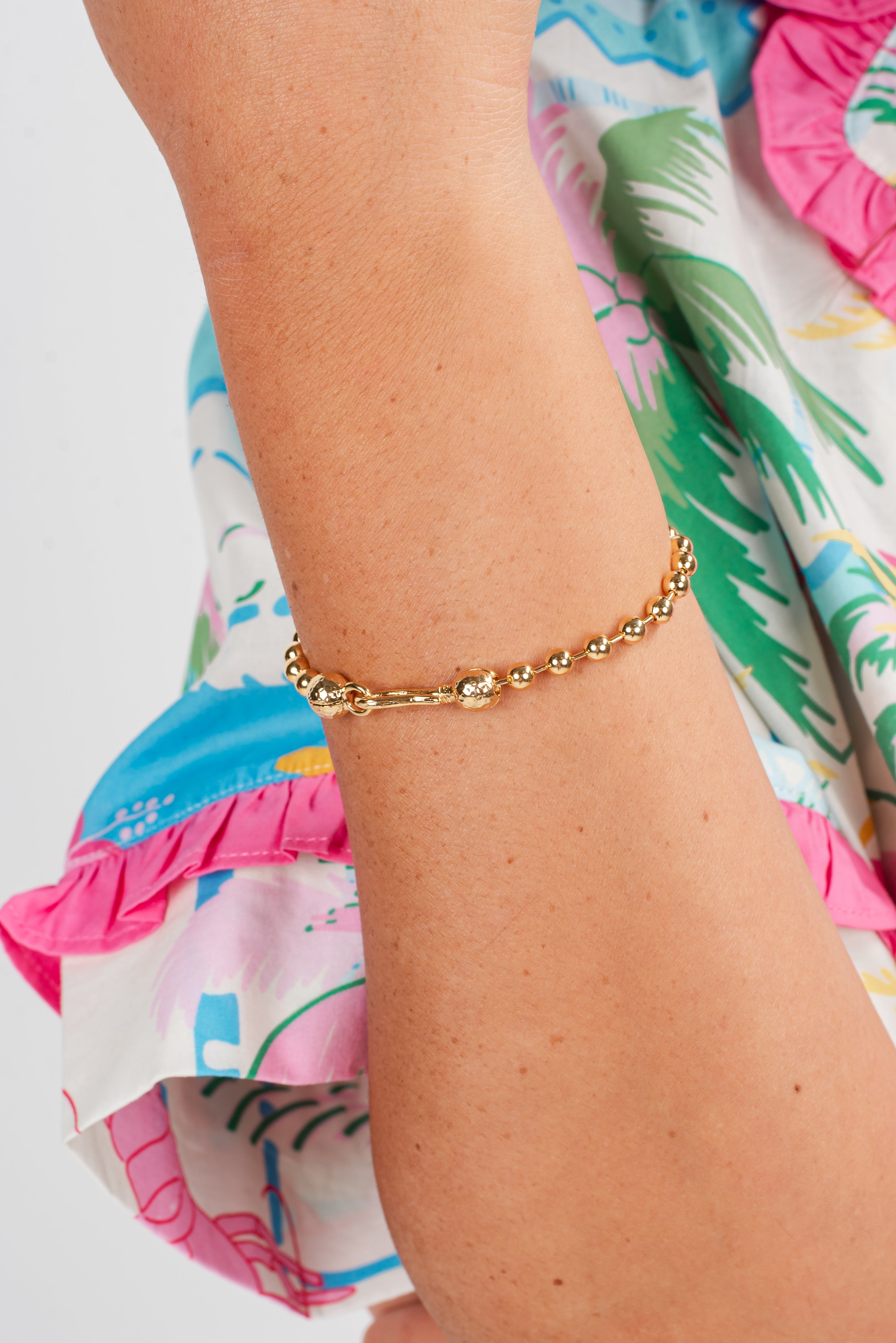 Gold bracelet on a wrist with a colorful palm tree patterned garment