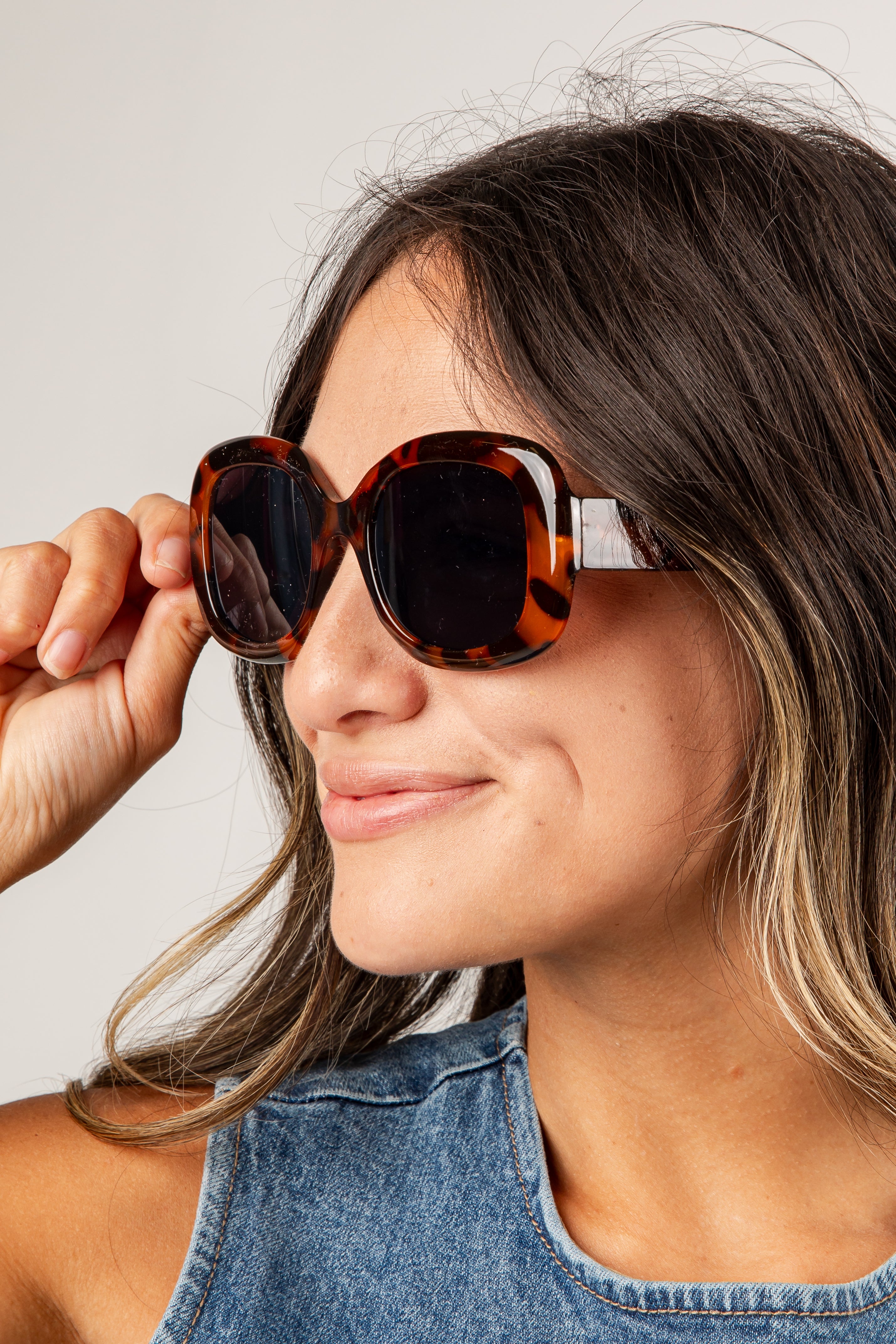 Woman wearing tortoiseshell sunglasses with a neutral background