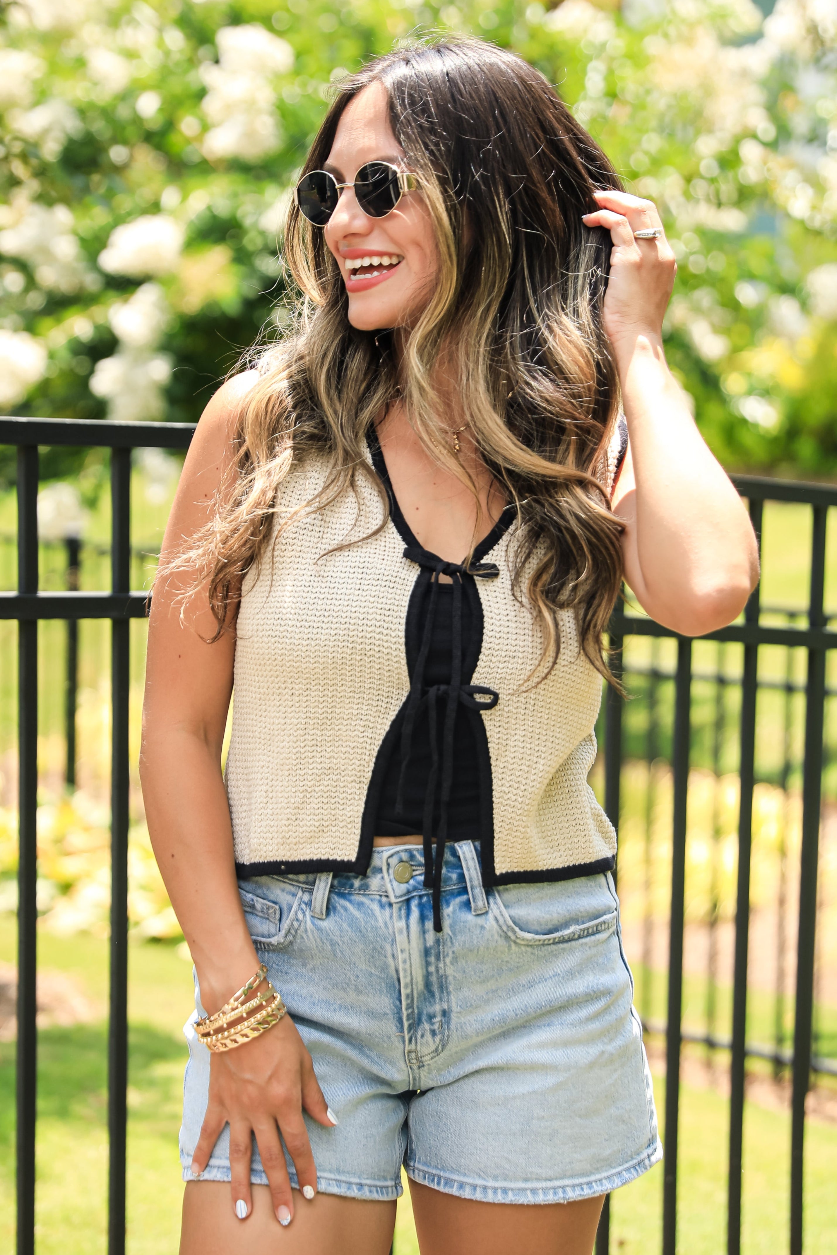 Woman in a light-colored top and denim shorts standing outdoors with greenery in the background