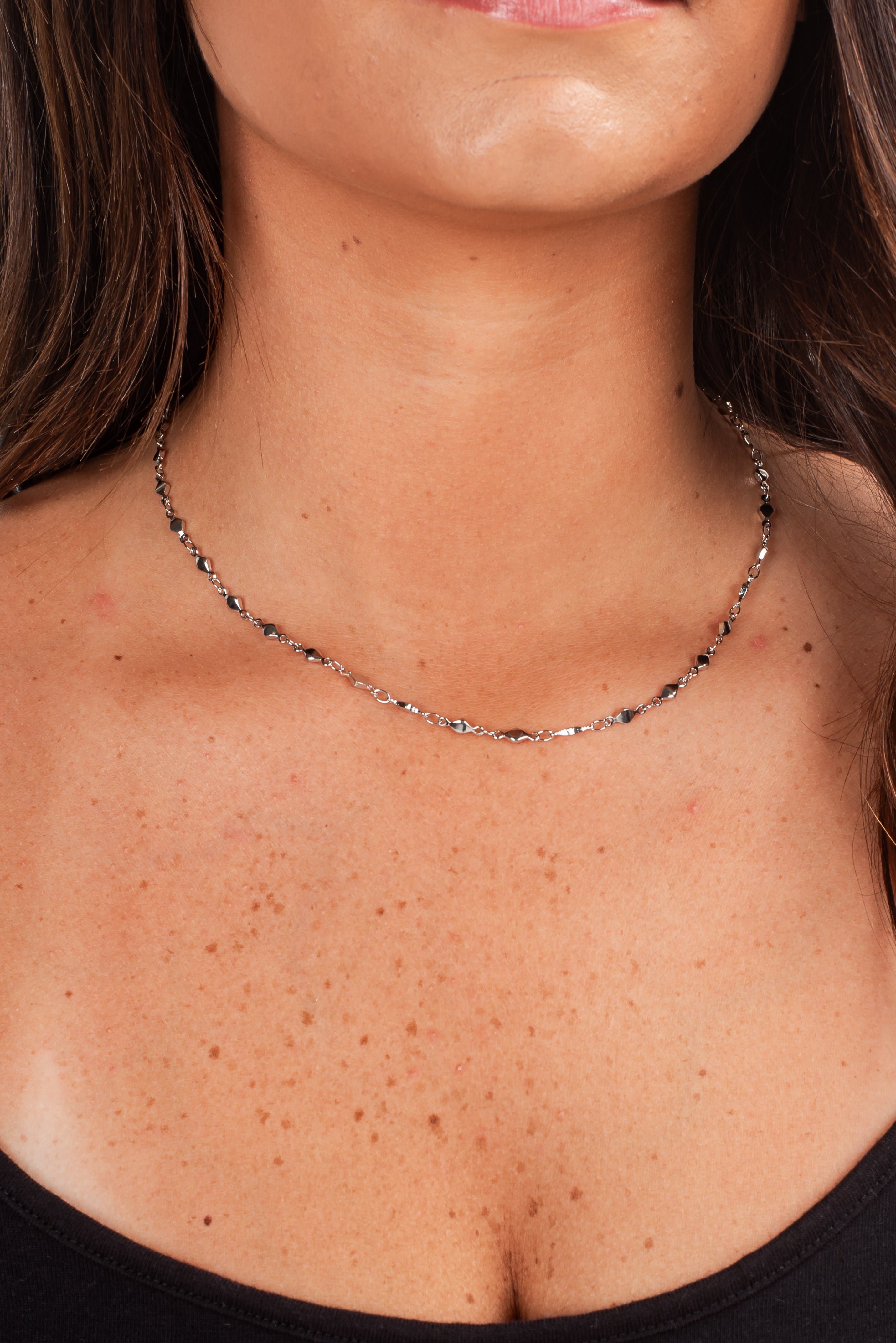 Close-up of a person wearing a silver necklace with a blurred background