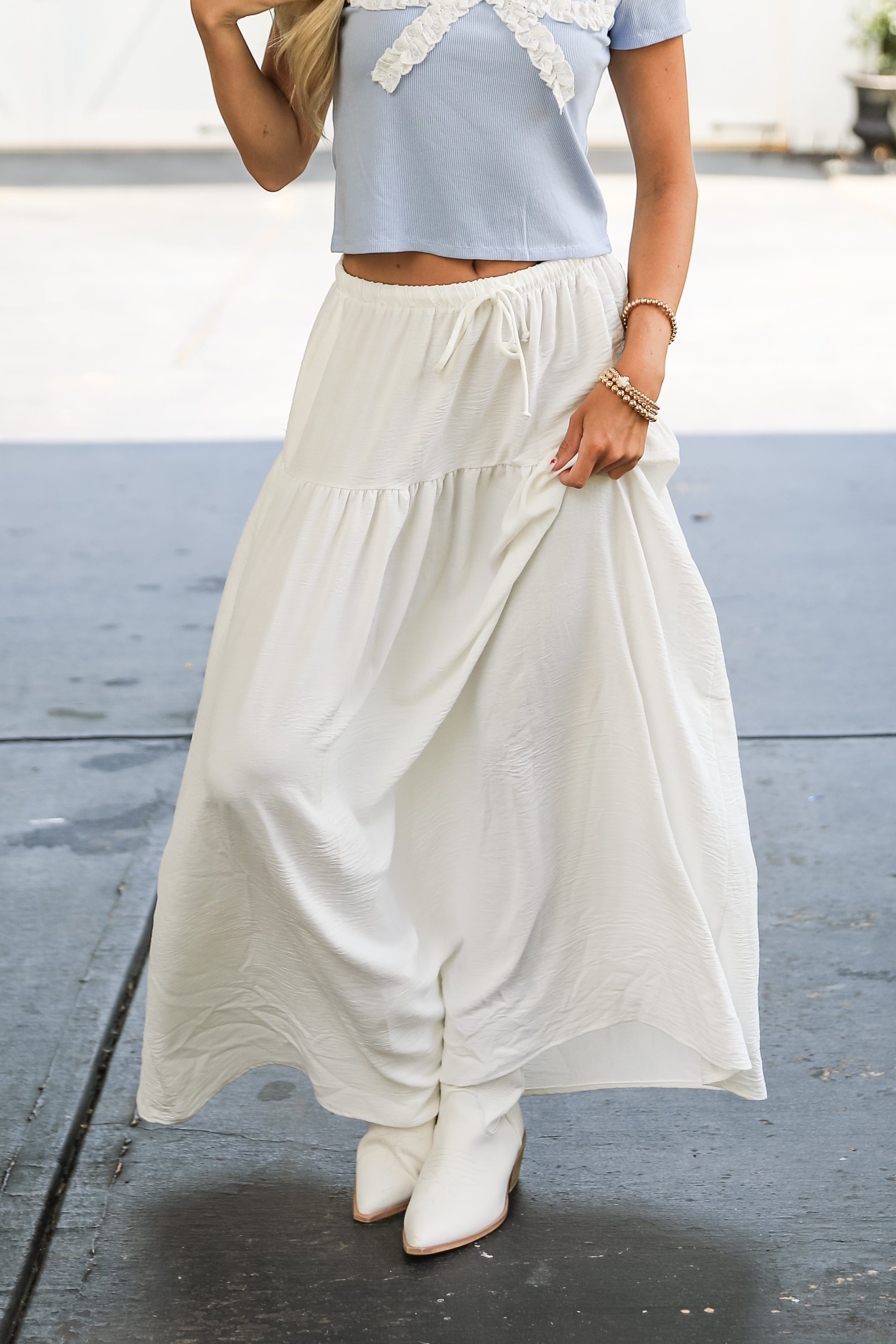 Person wearing a light blue top and white skirt on a street.