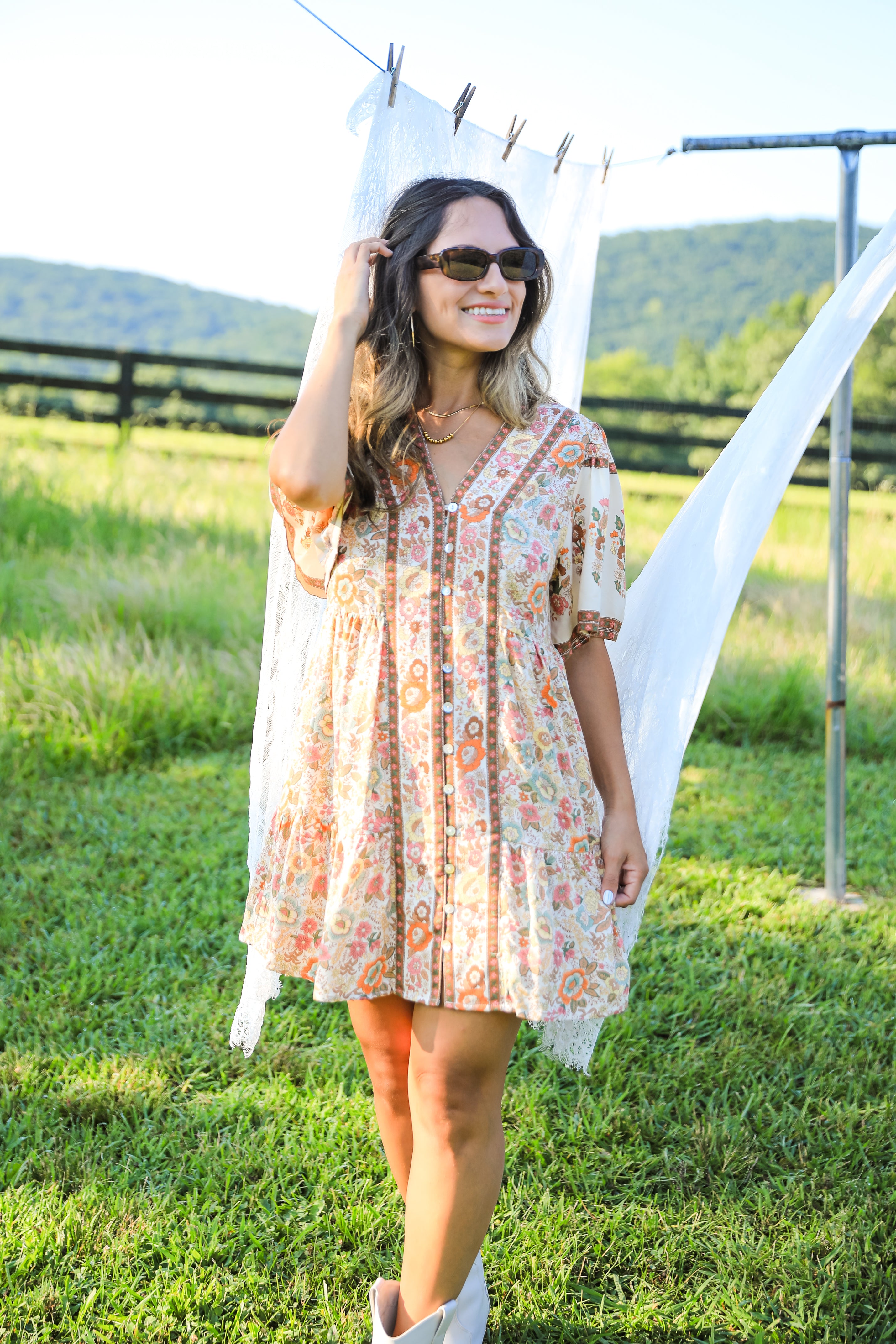 Woman in a floral dress standing in a grassy field with mountains in the background
