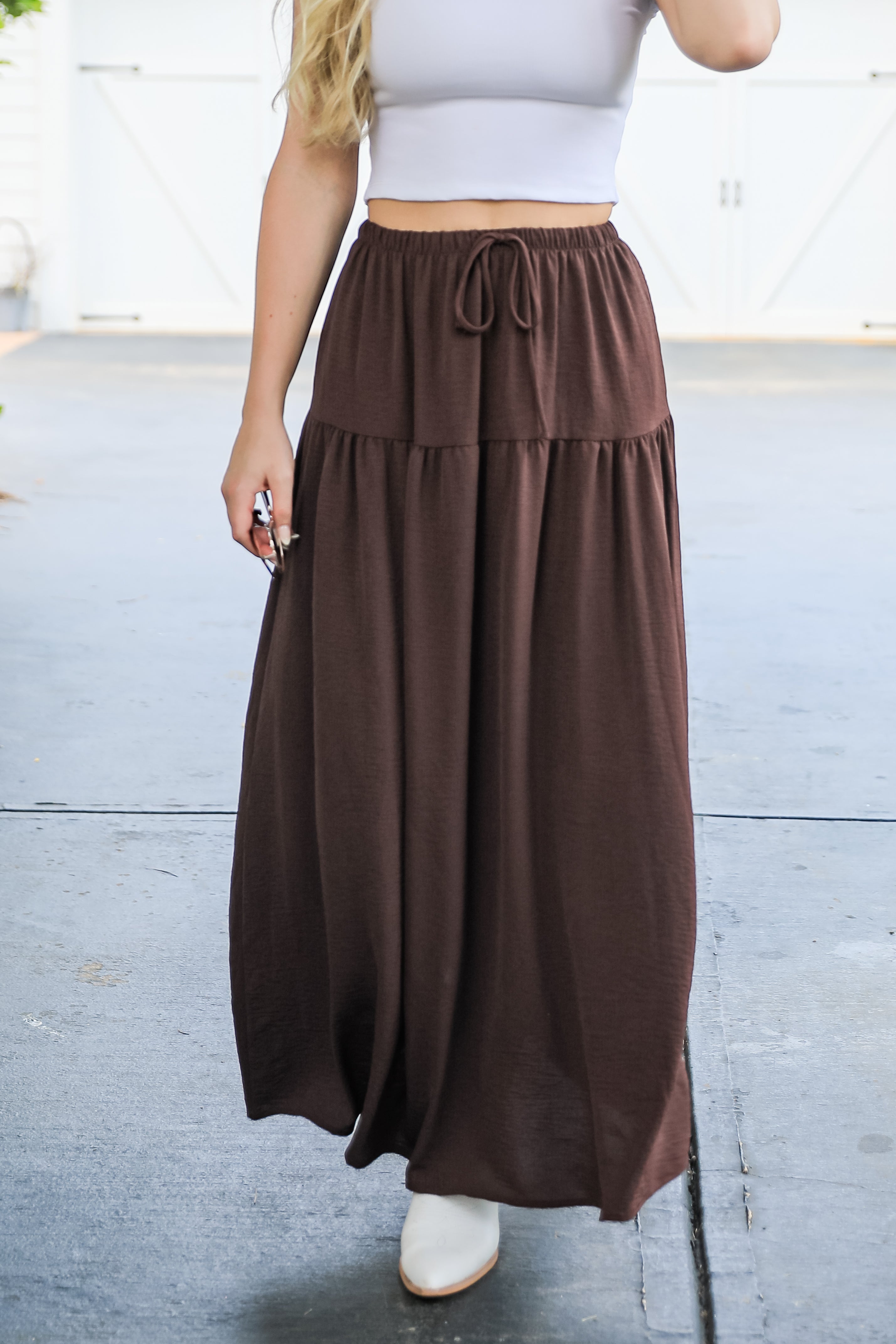 Person wearing a brown maxi skirt with a white top and shoes on a light background