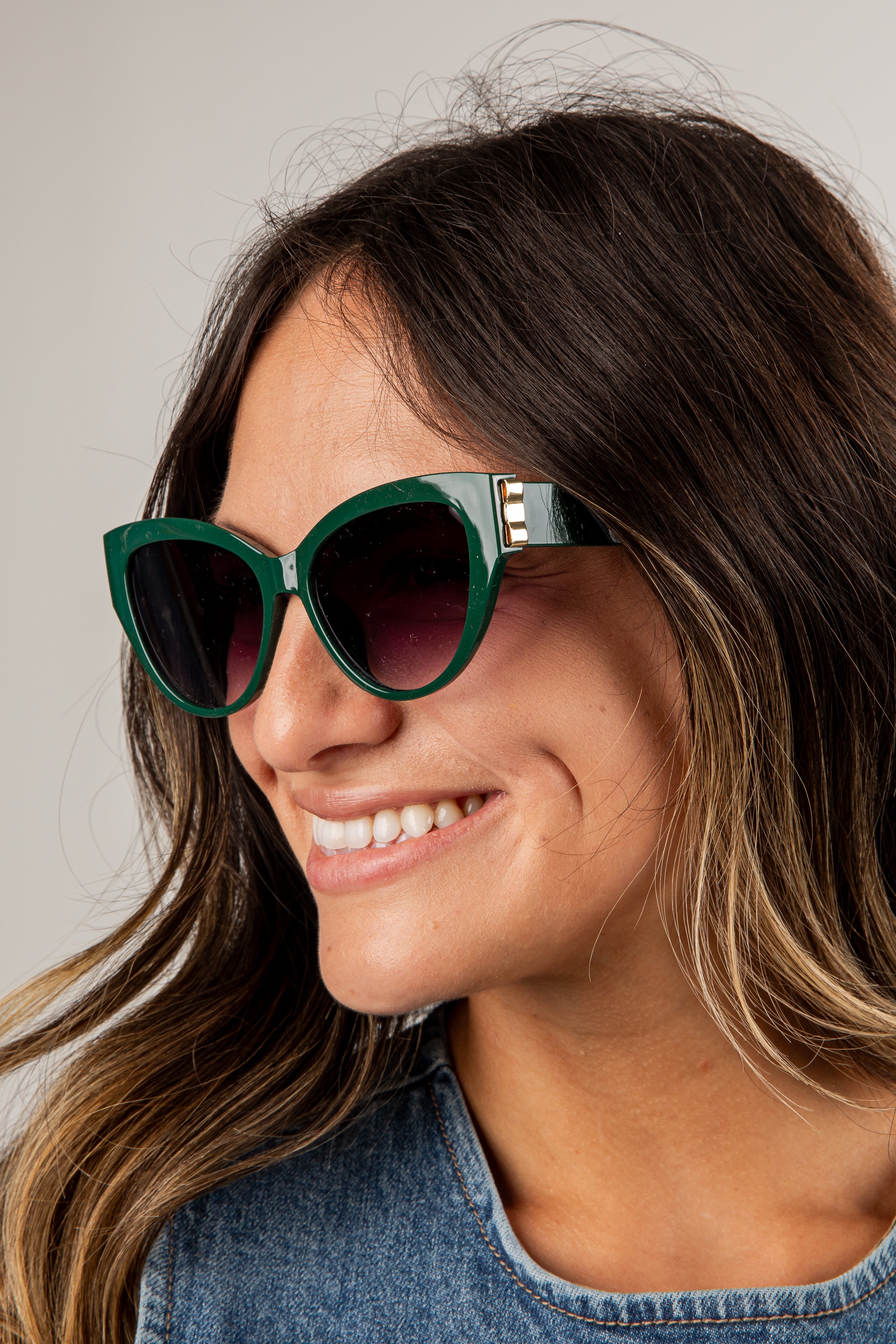 Woman wearing green sunglasses with a neutral background