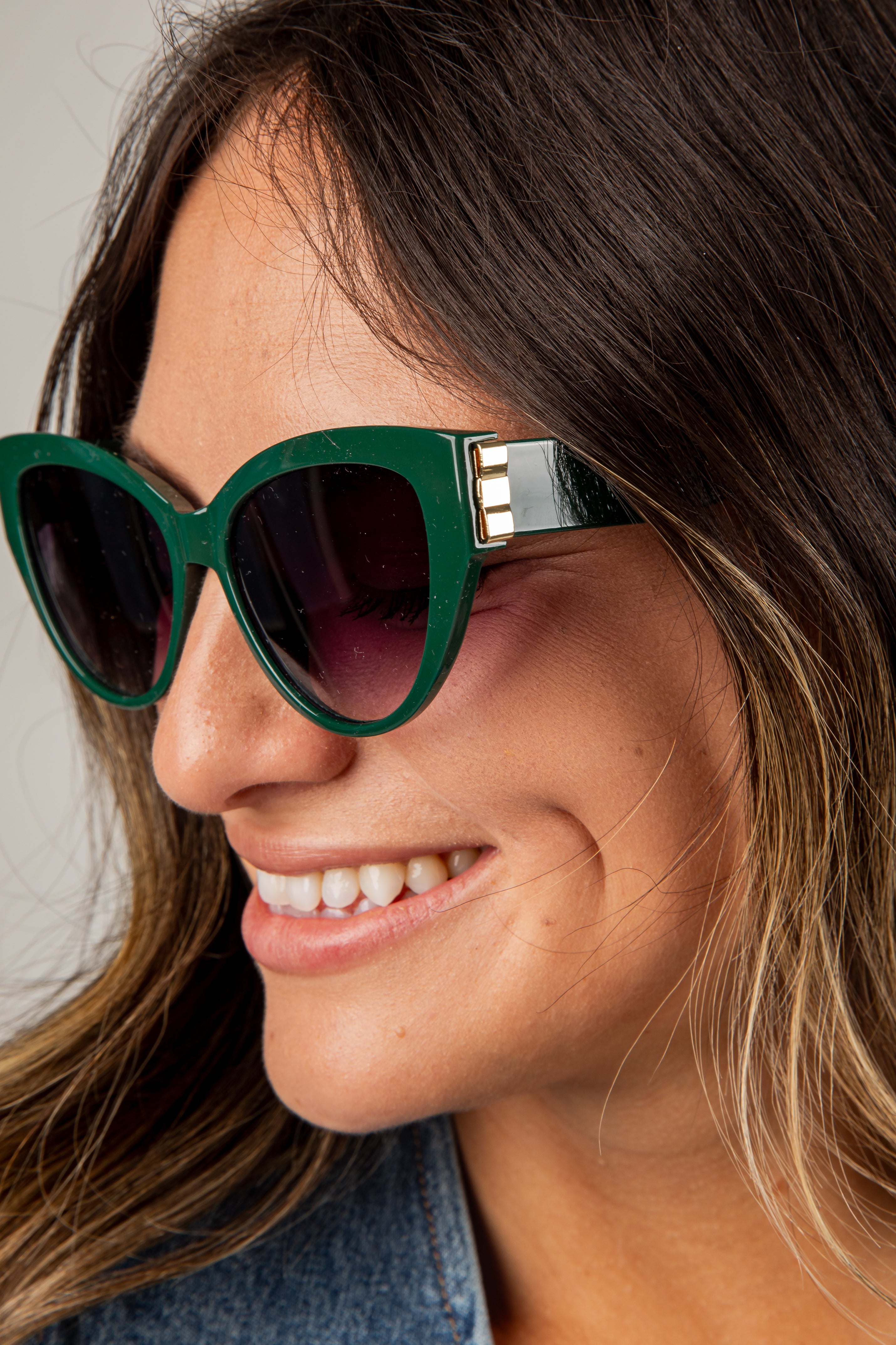 Woman wearing green cat-eye sunglasses with a neutral background