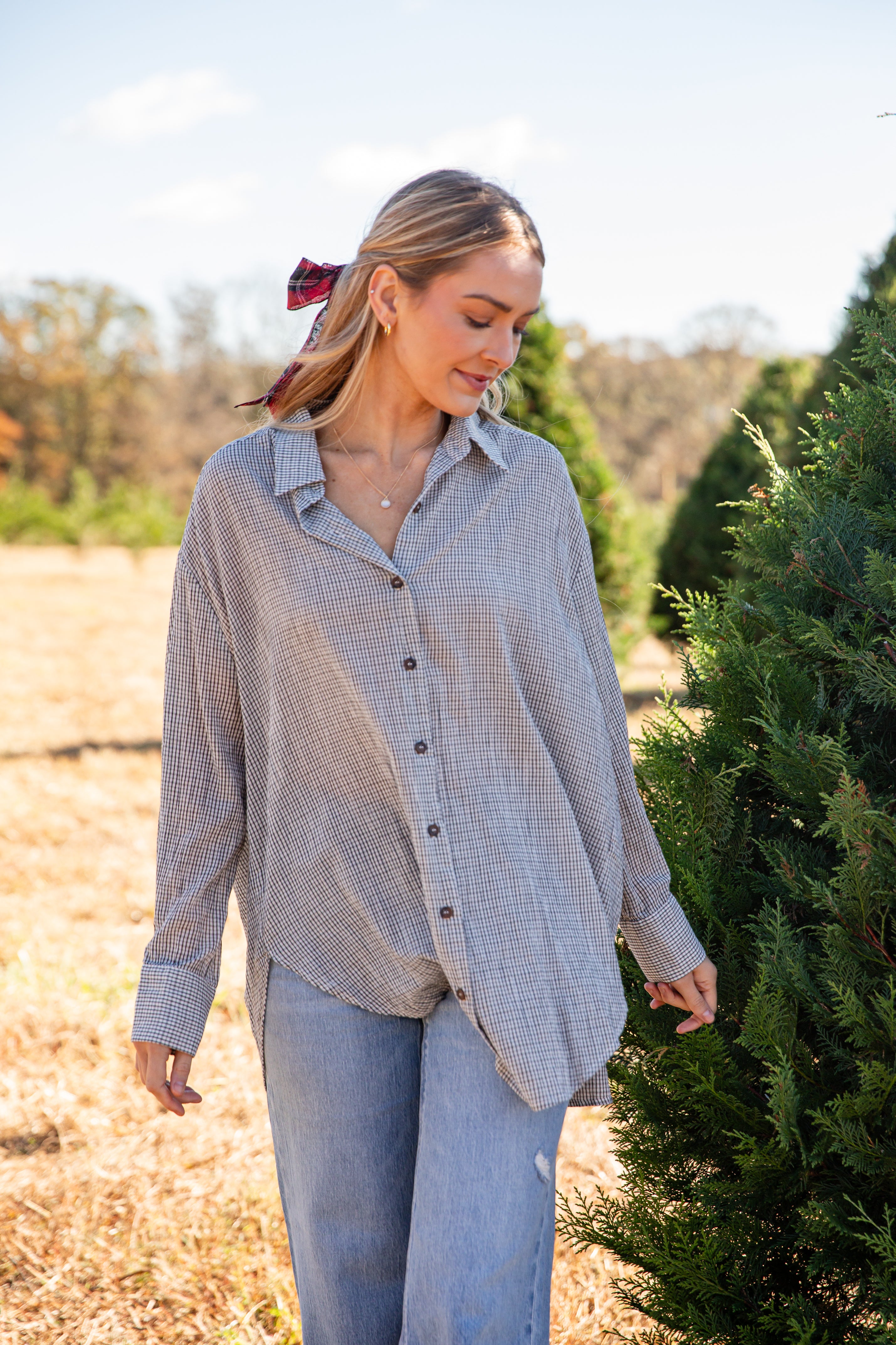 Woman wearing a plaid shirt and jeans standing among trees
