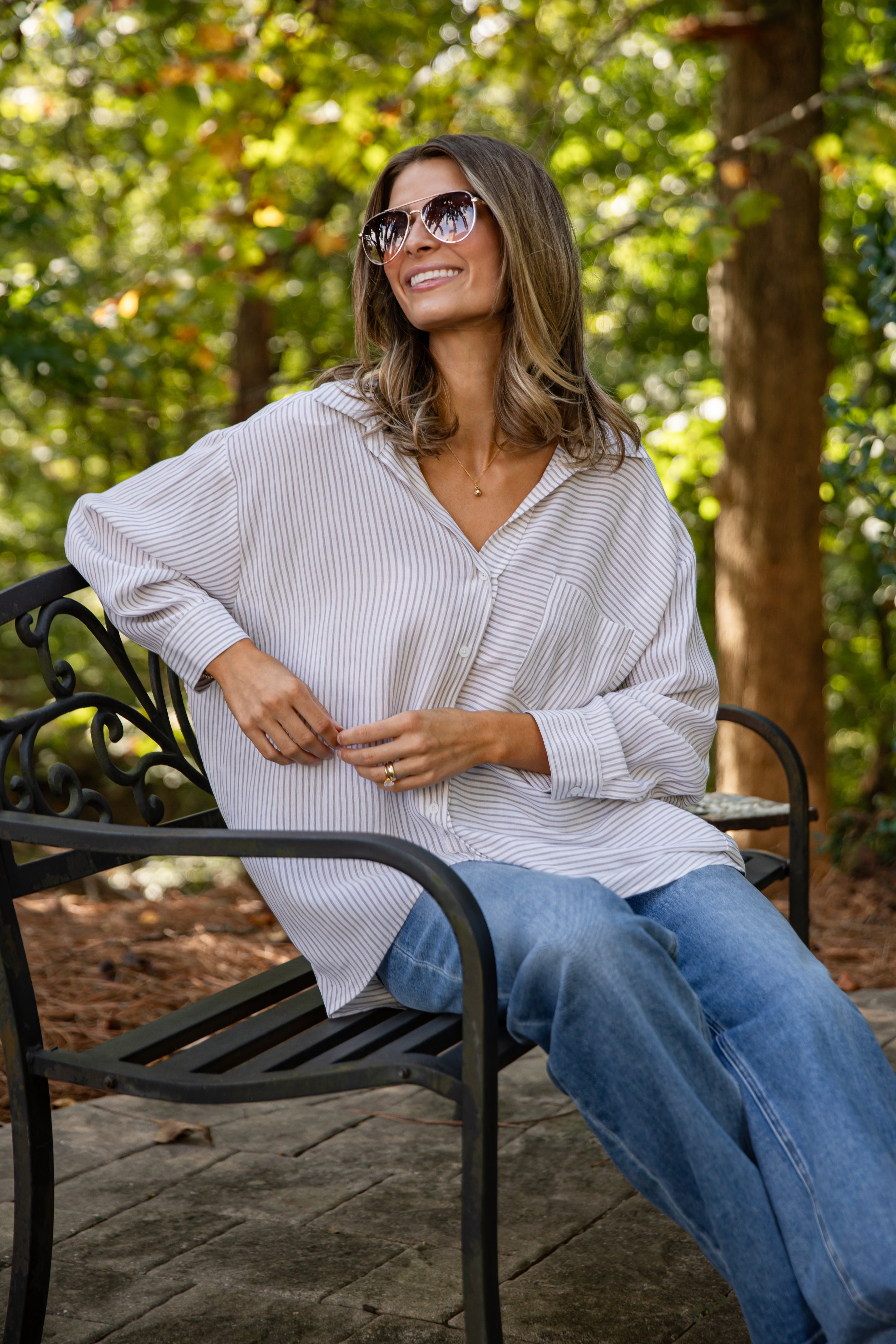 Woman sitting on a bench outdoors wearing sunglasses and a light-colored shirt.