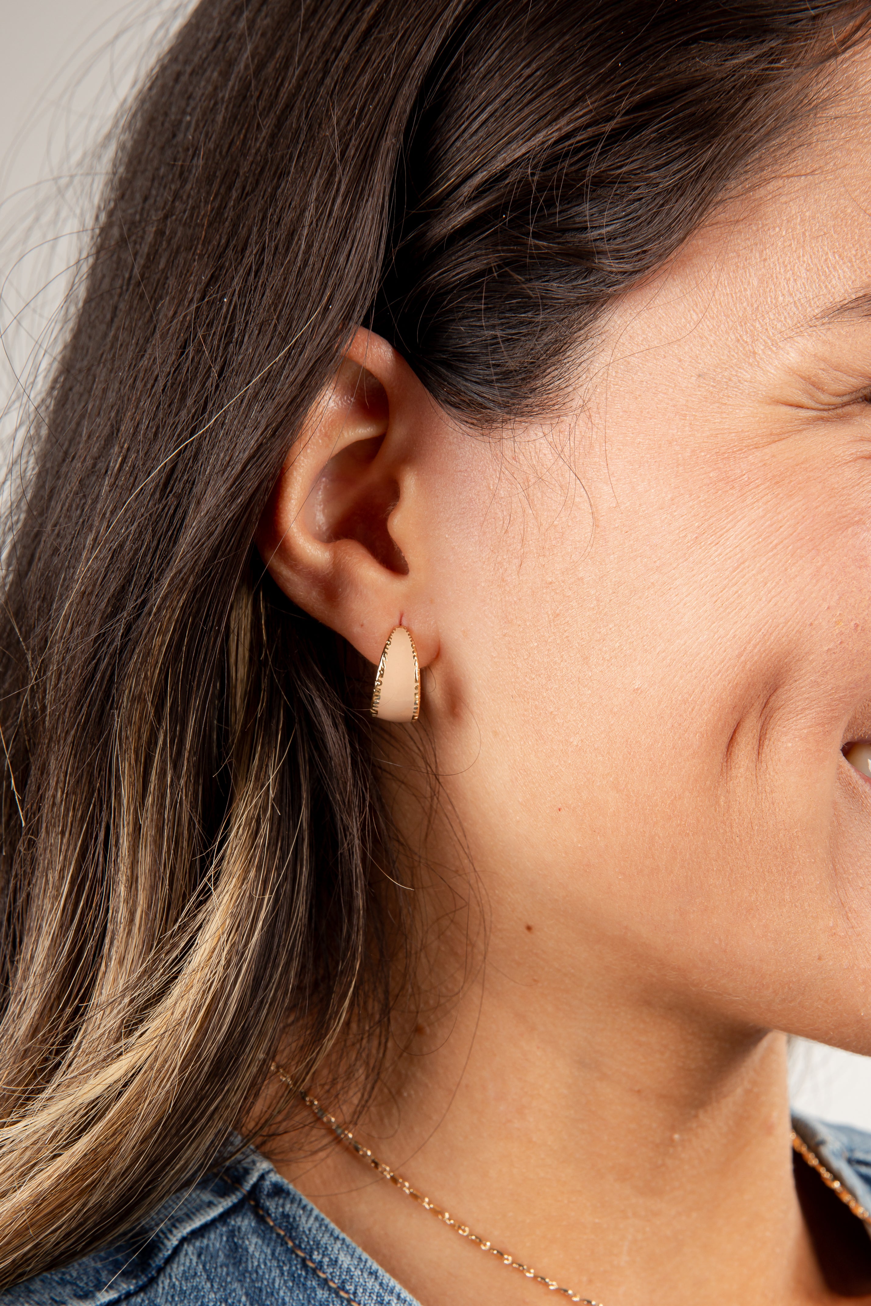 Close-up of a person wearing a small beige earring.