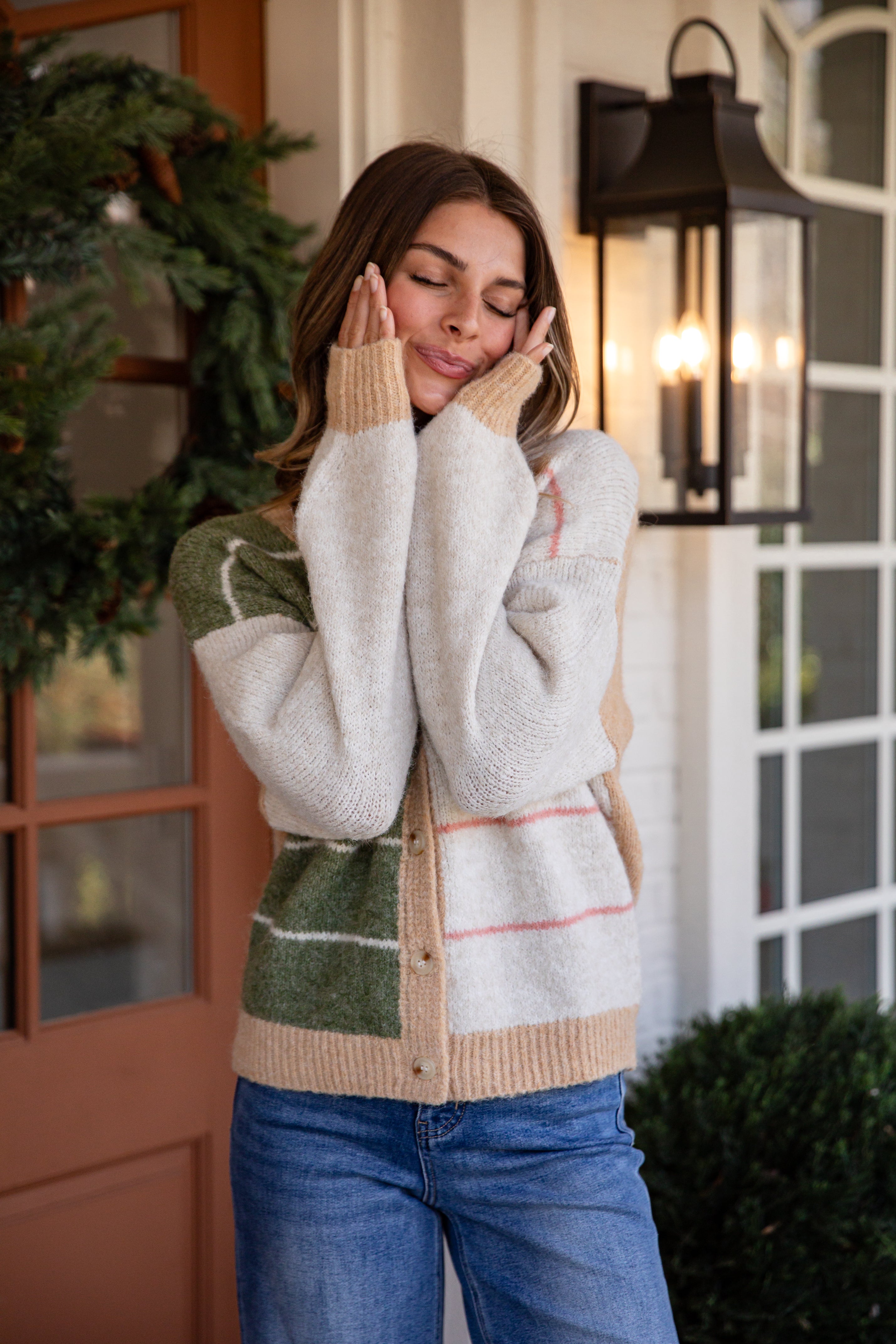 Woman wearing a patterned cardigan in front of a door with a wreath.