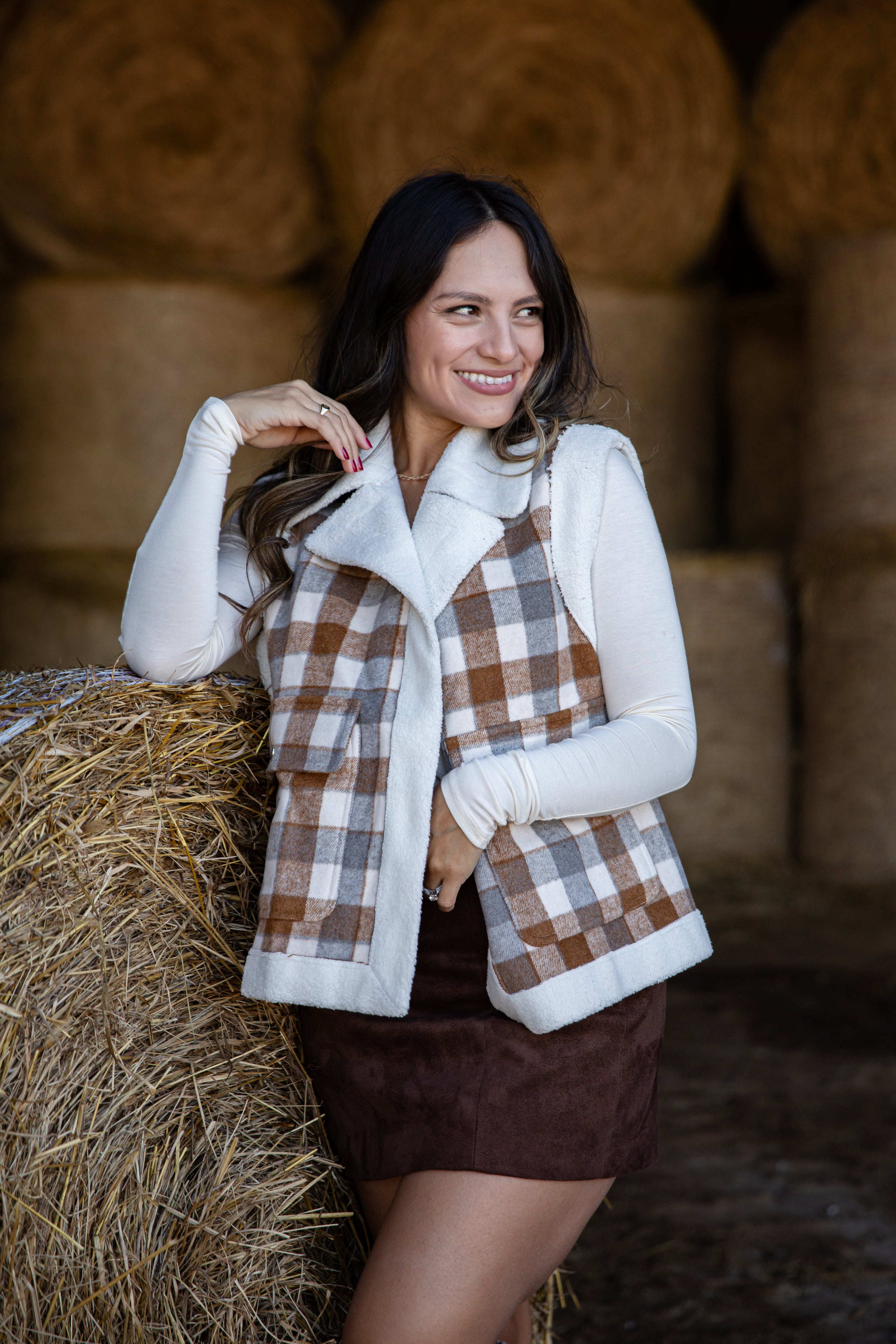 Woman in a plaid vest and white shirt standing in front of hay bales
