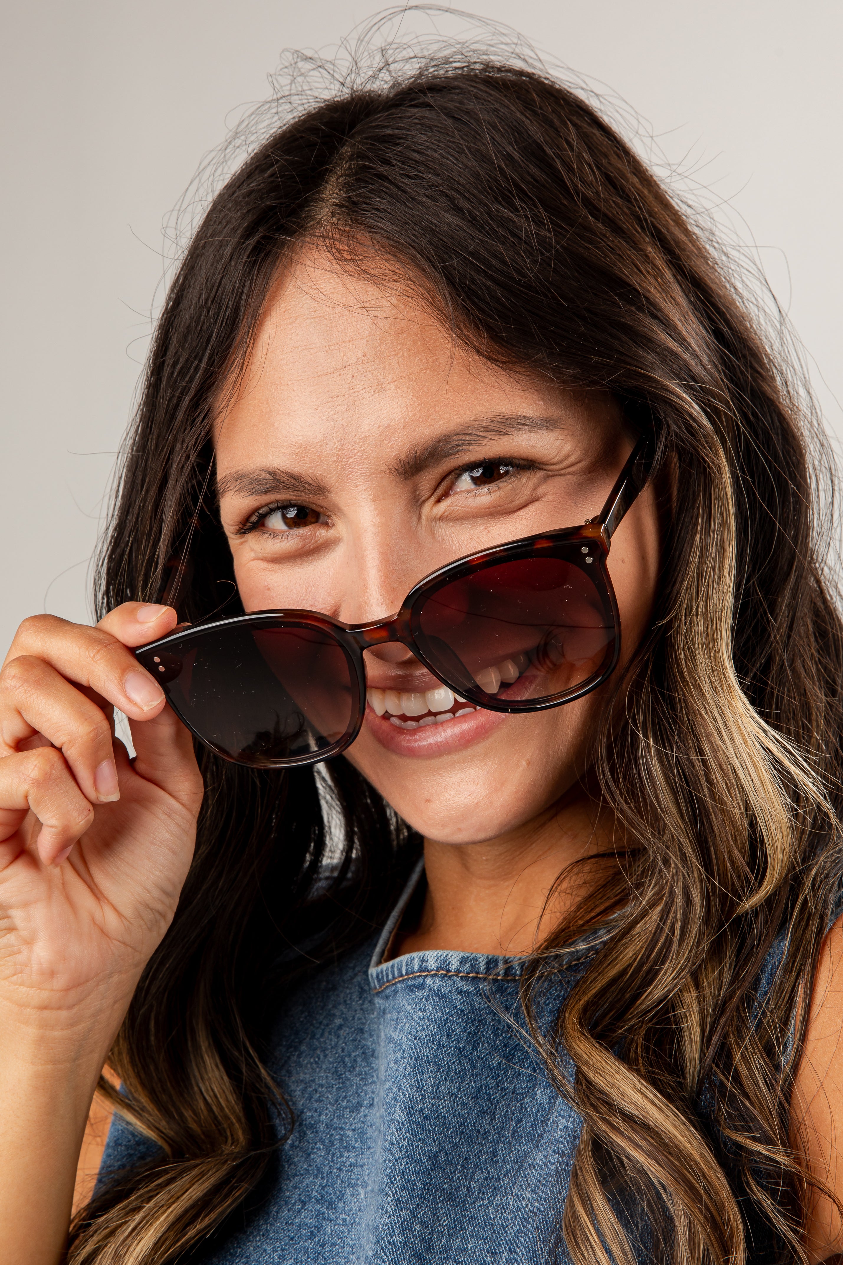 Woman holding sunglasses up to her face with a neutral background