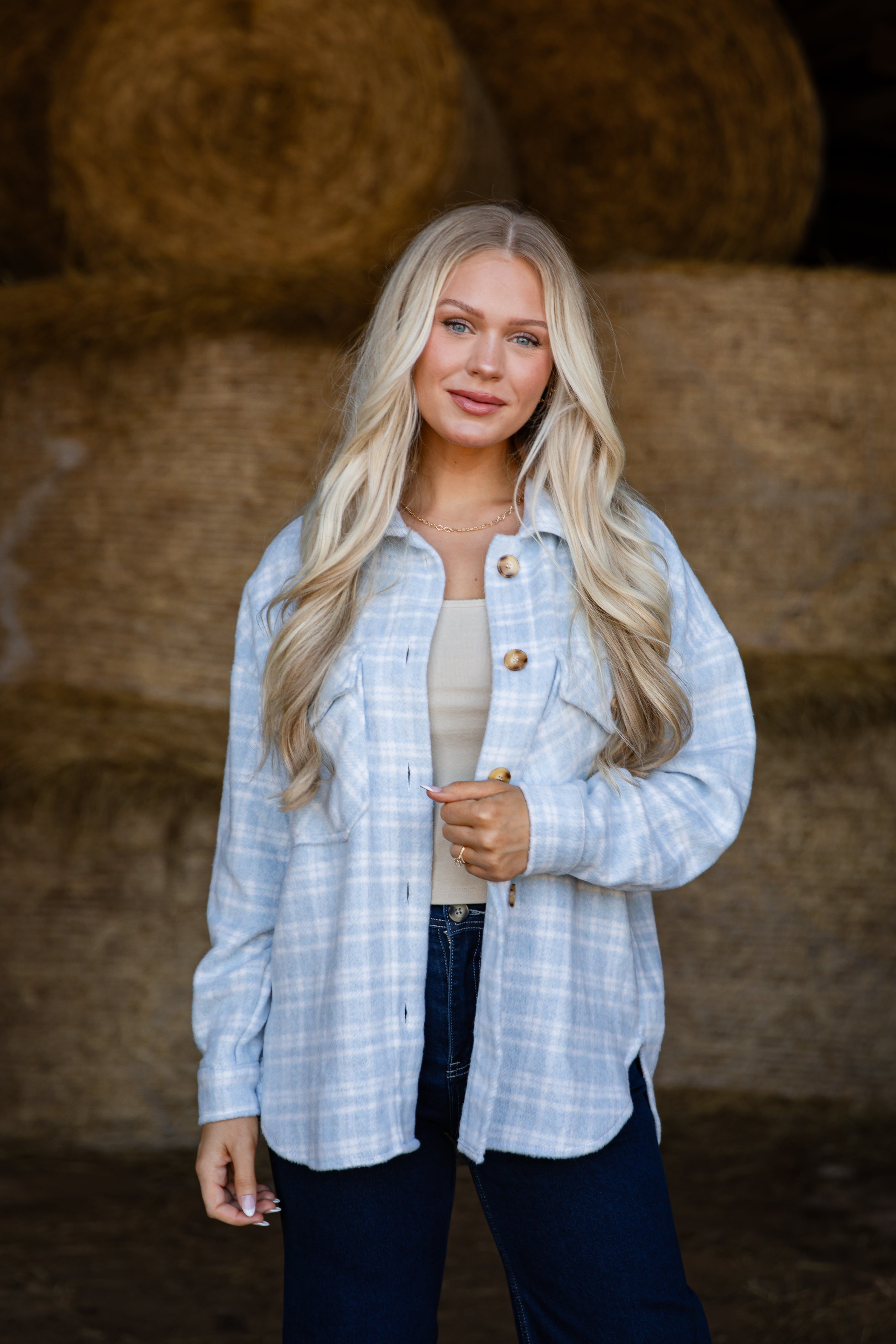 Woman wearing a light blue plaid shirt in front of hay bales