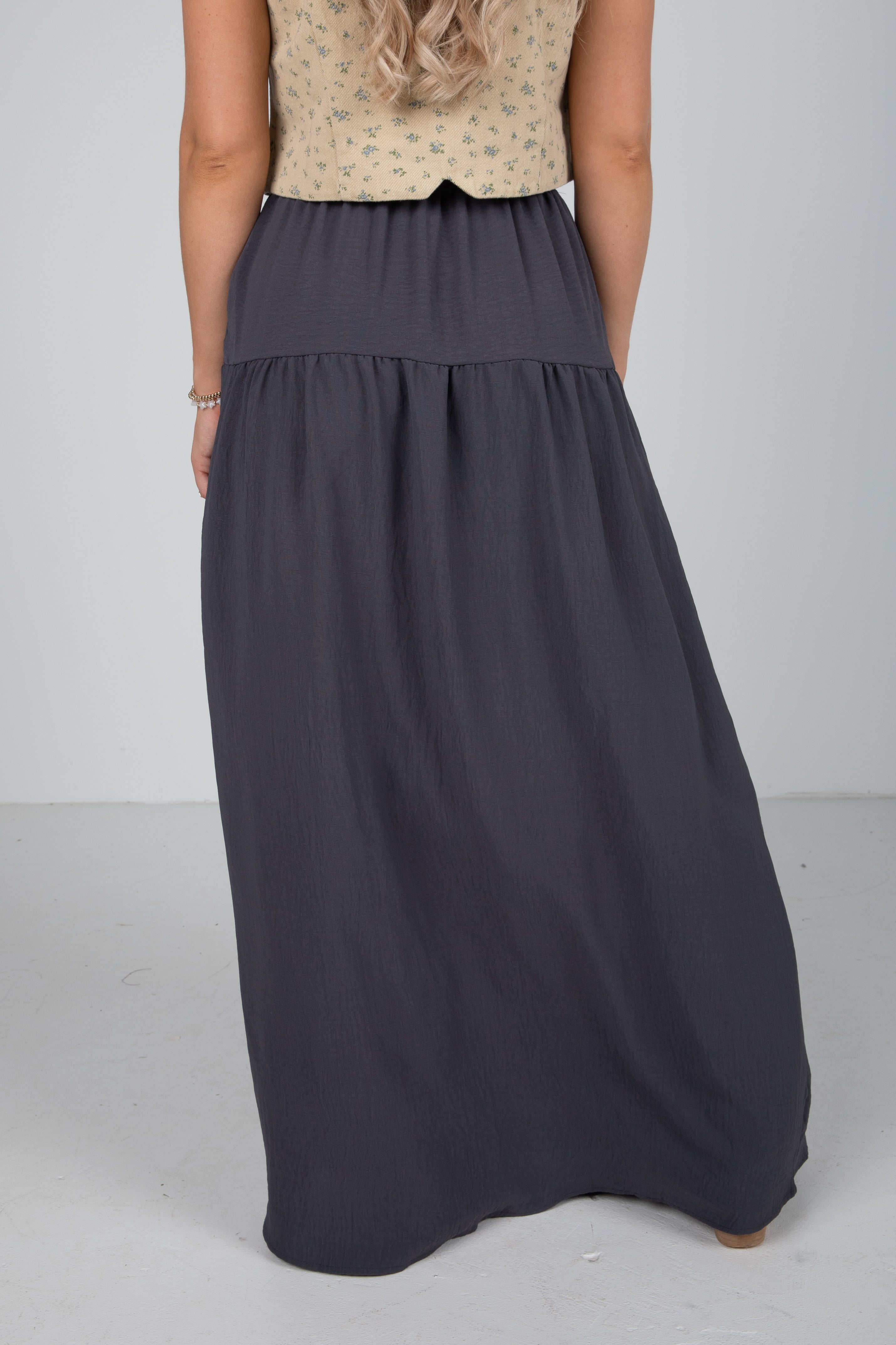 Person wearing a long dark gray skirt on a plain background