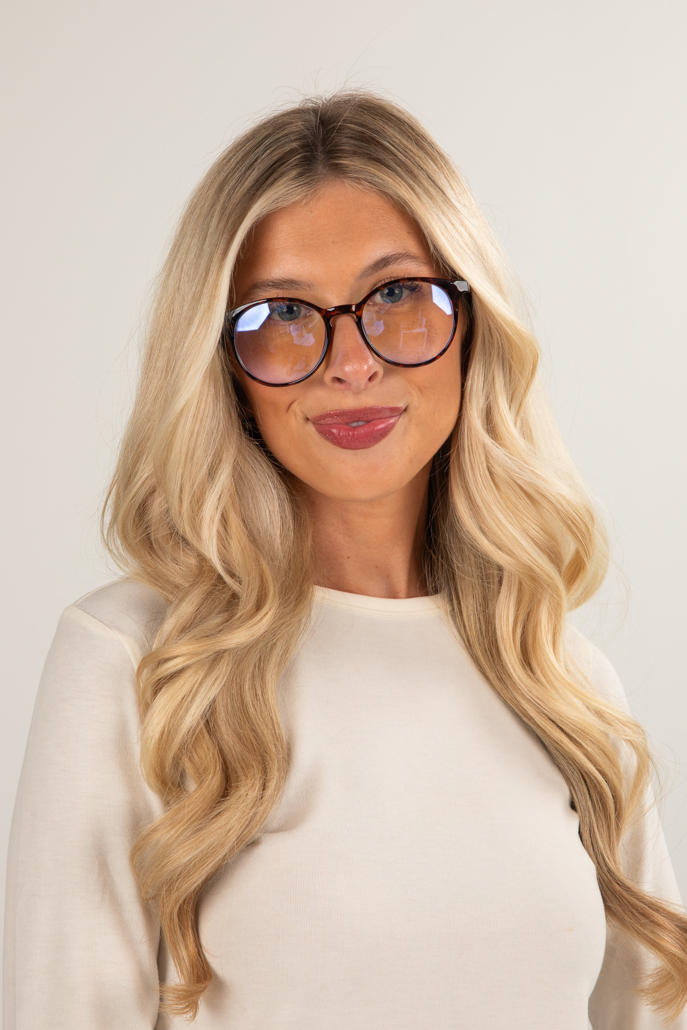 Woman with long blonde hair and glasses wearing a white top against a plain background