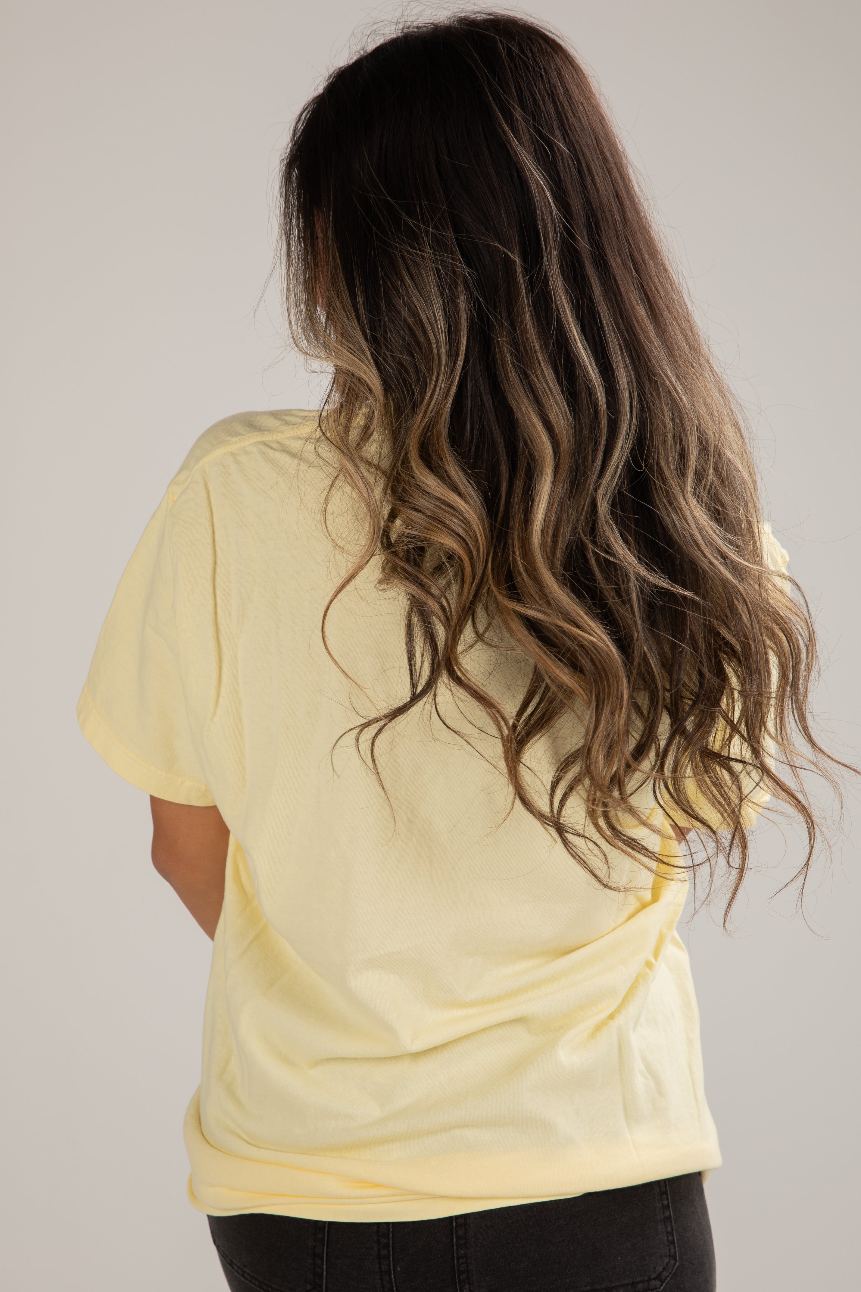 Woman wearing a yellow t-shirt with long, wavy hair on a plain background