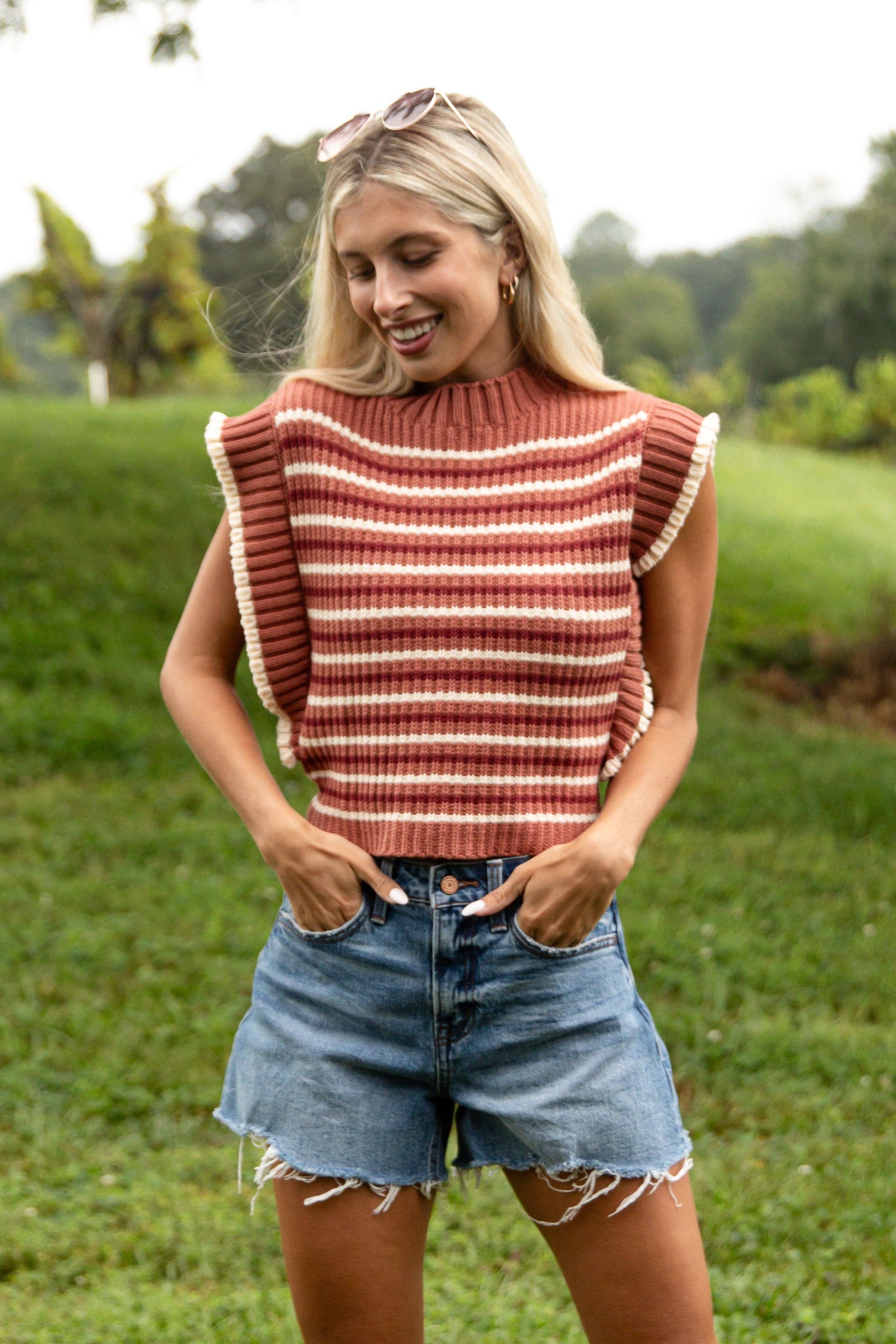 Woman wearing a striped top and denim shorts standing in a grassy outdoor area.