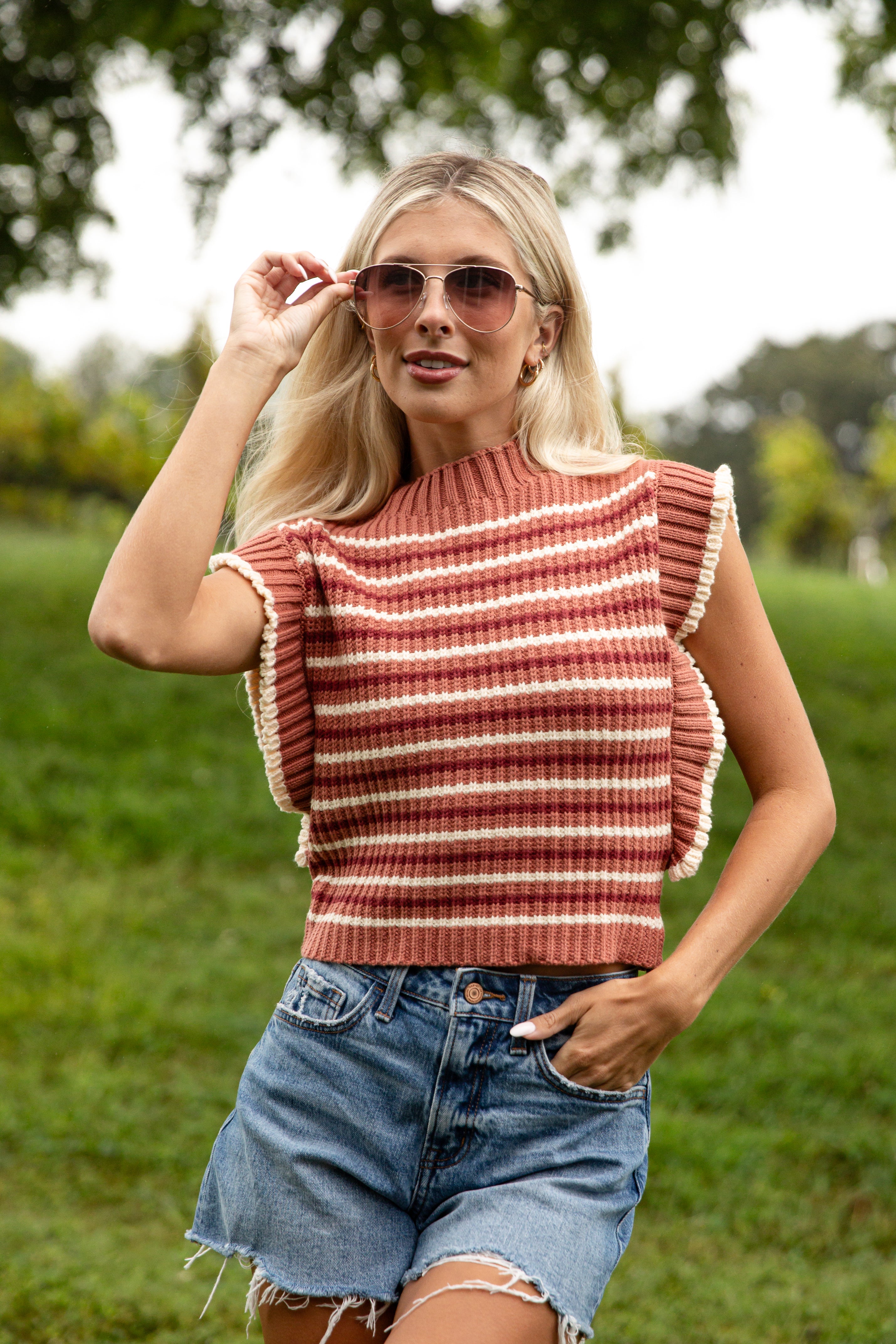 Woman wearing a striped sleeveless top and denim shorts outdoors.