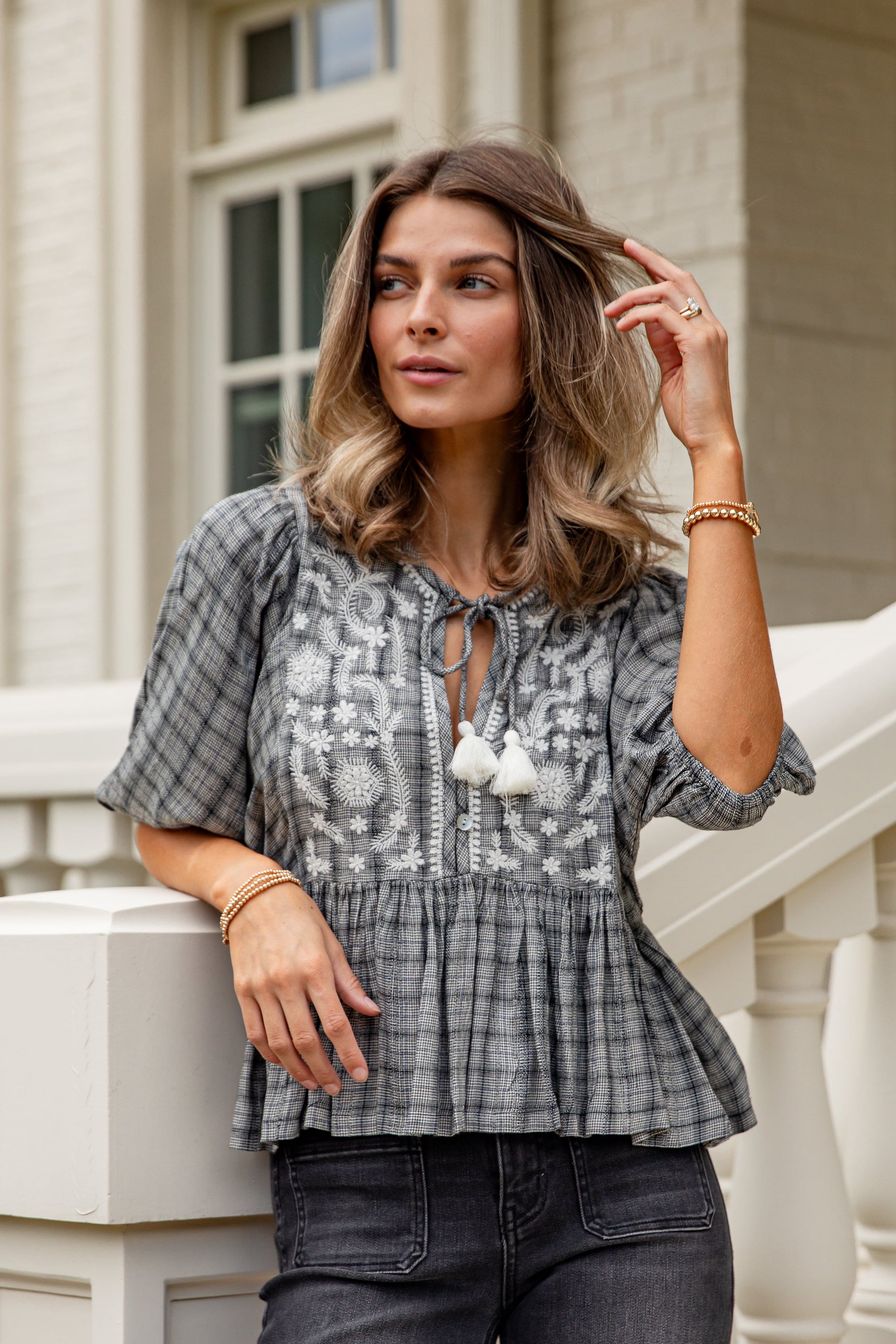 Woman wearing a patterned blouse and jeans standing on a staircase.