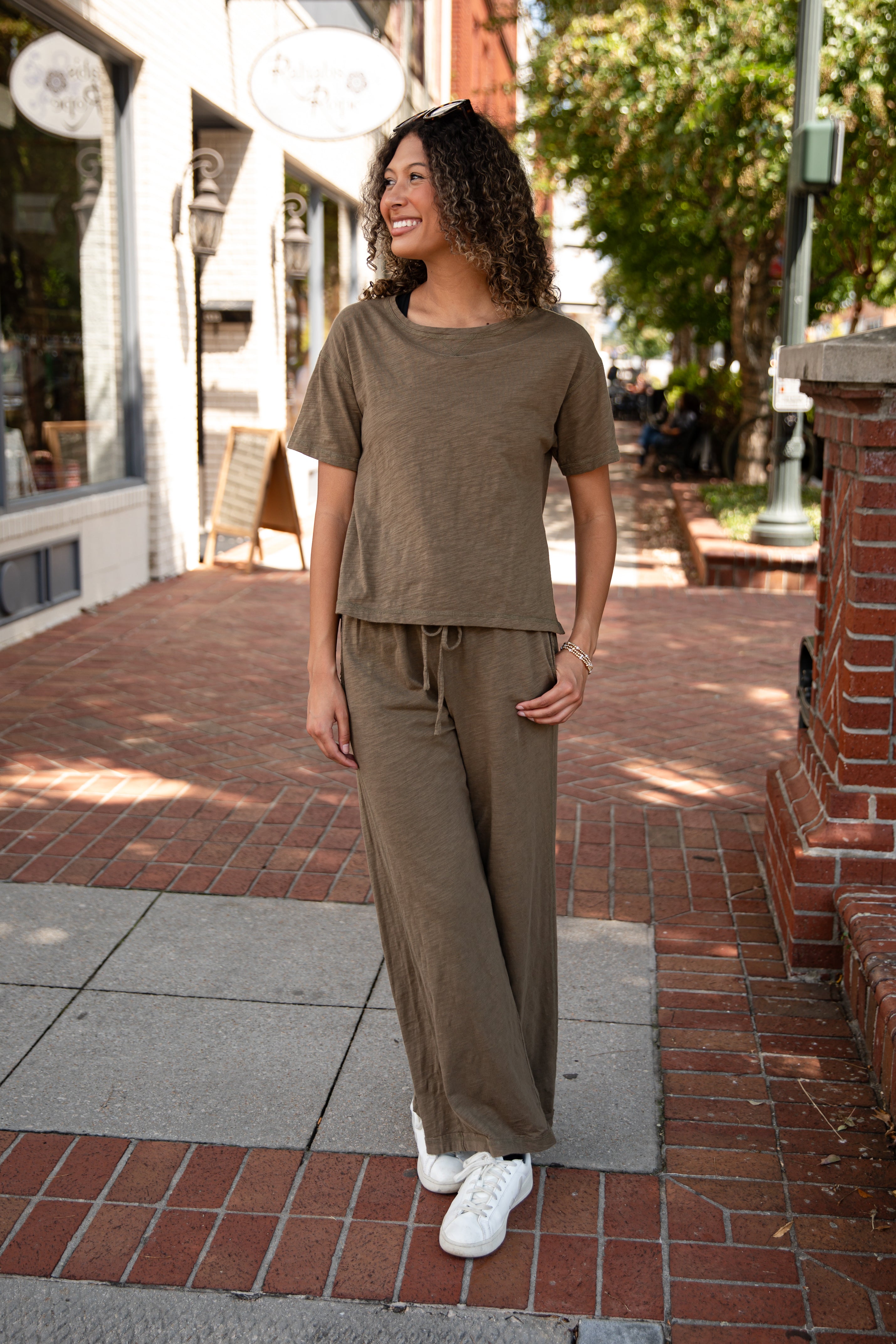 Woman in a brown outfit standing on a sidewalk with shops in the background