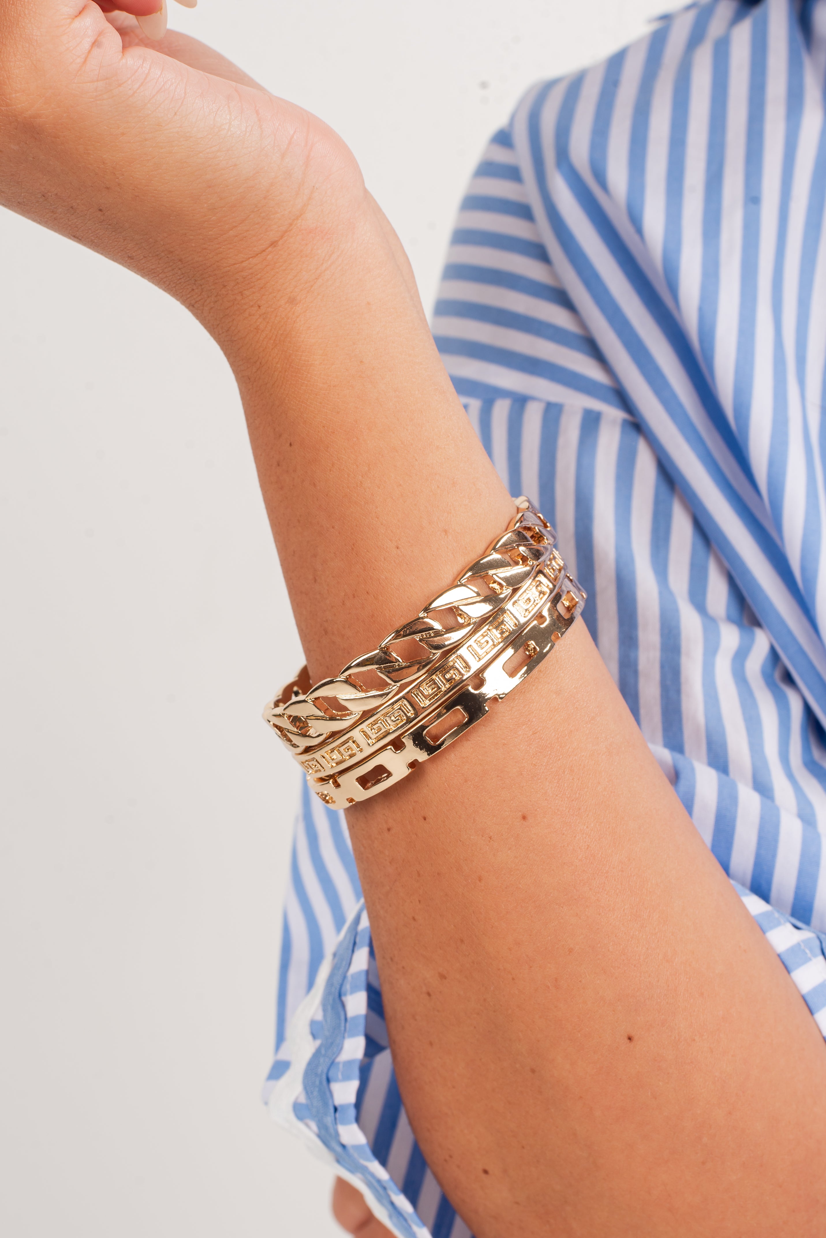 Gold bracelets on a wrist with a blue and white striped shirt