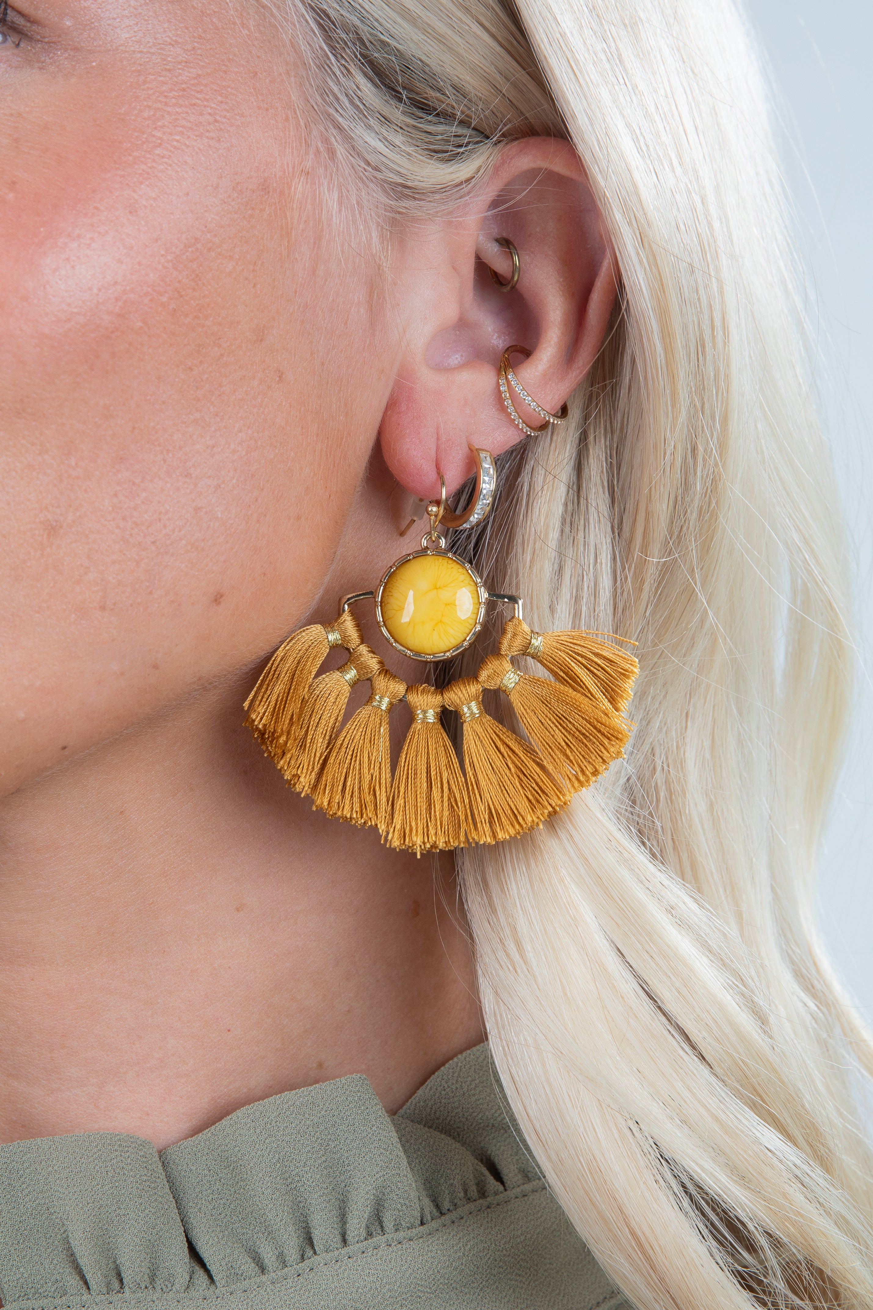 Close-up of a person wearing a yellow tassel earring with a plain background