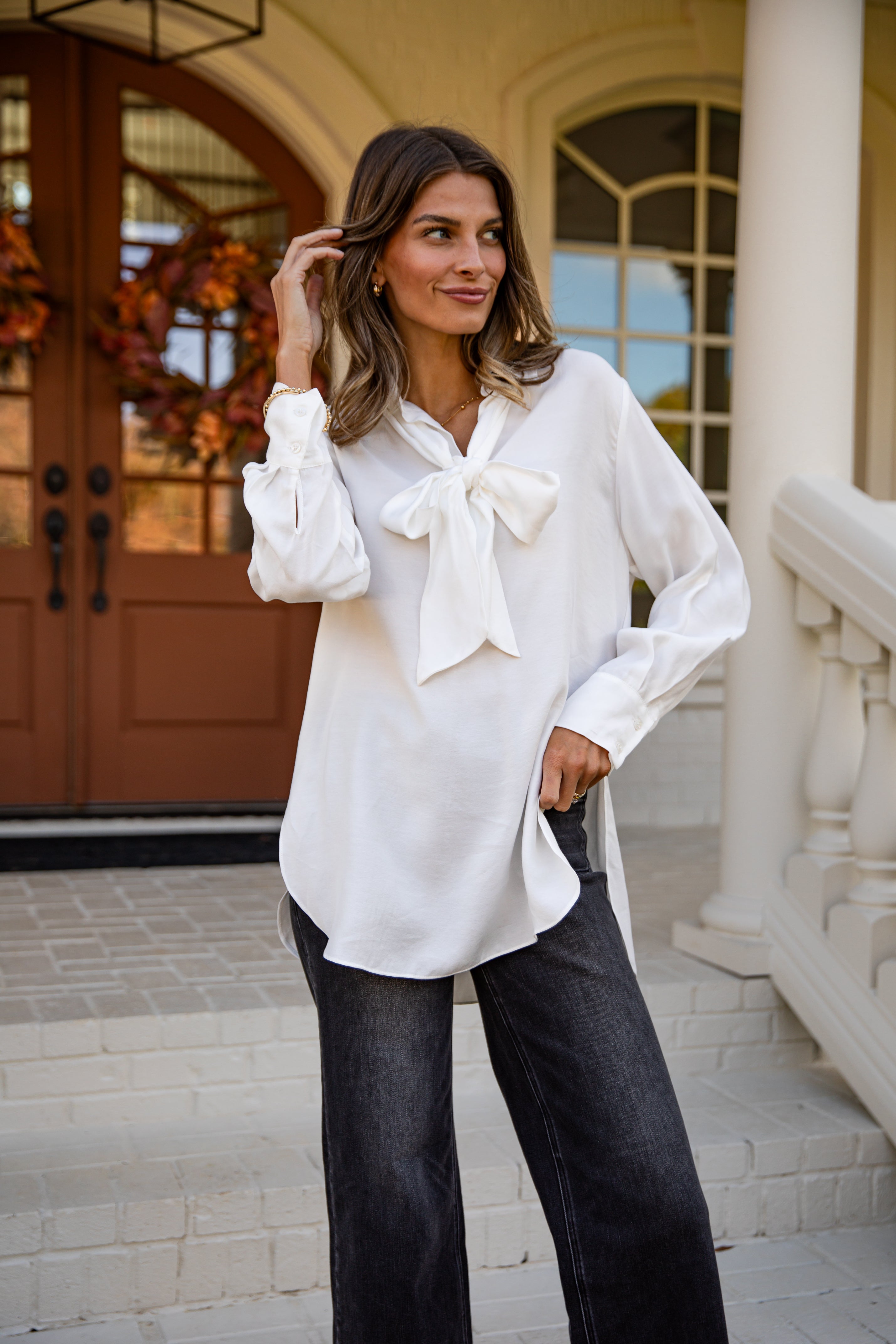 Woman wearing a white blouse with a bow tie and black pants standing in front of a building entrance.