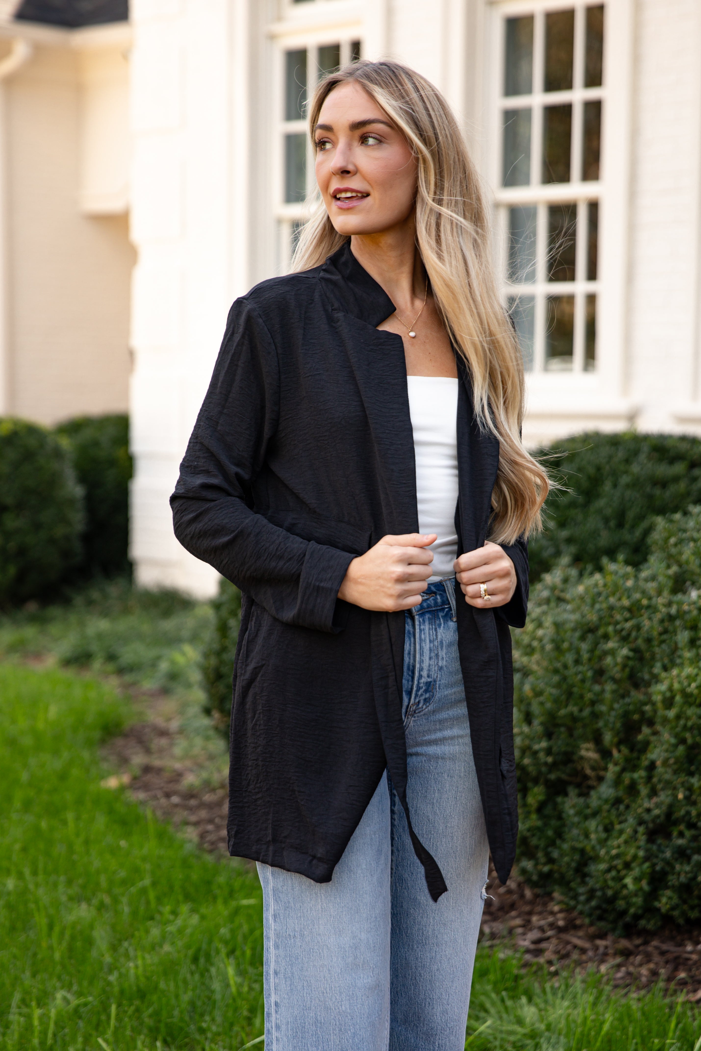 Woman wearing a black jacket, white top, and blue jeans outdoors.
