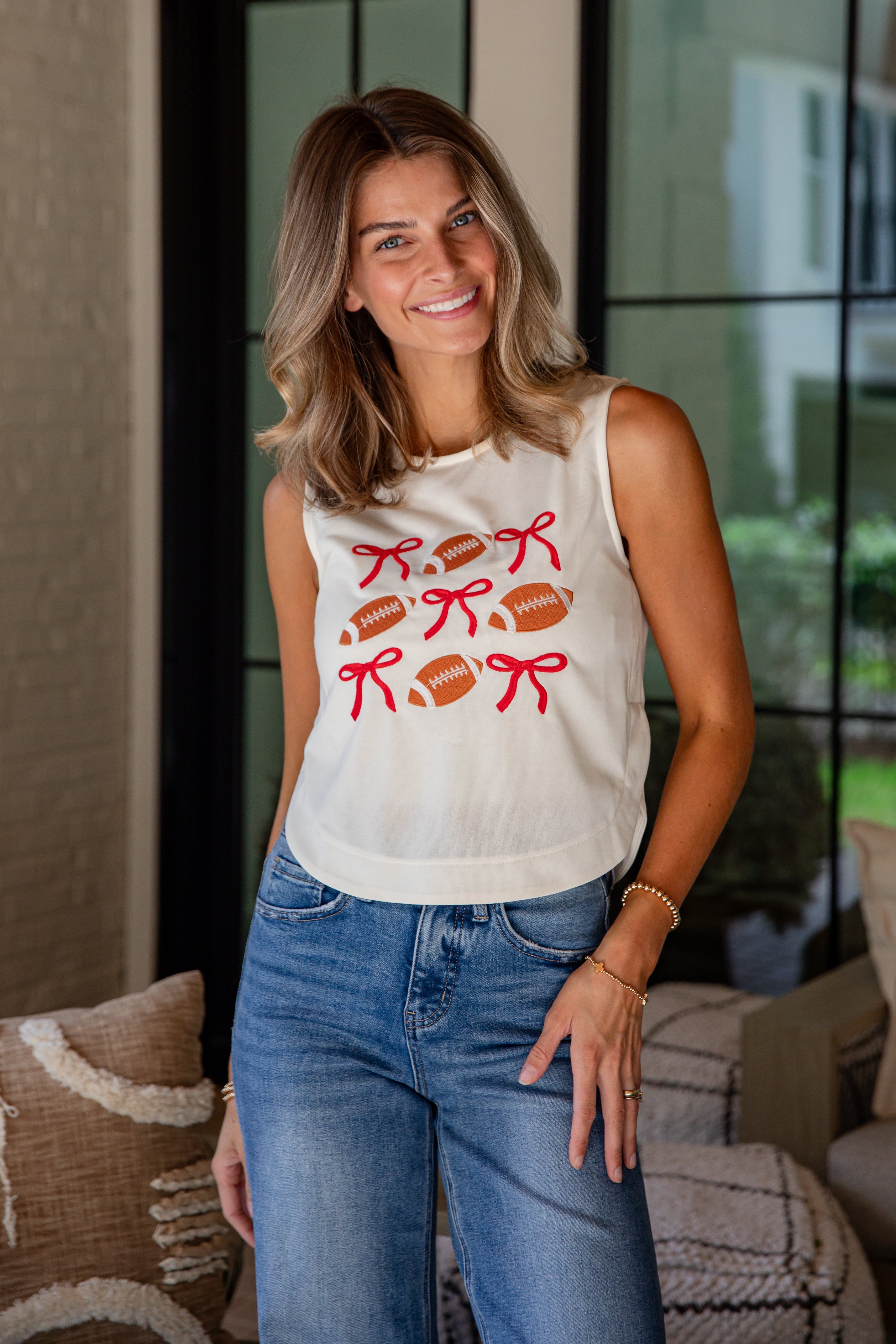 Woman wearing a white sleeveless shirt with red graphics and blue jeans indoors.