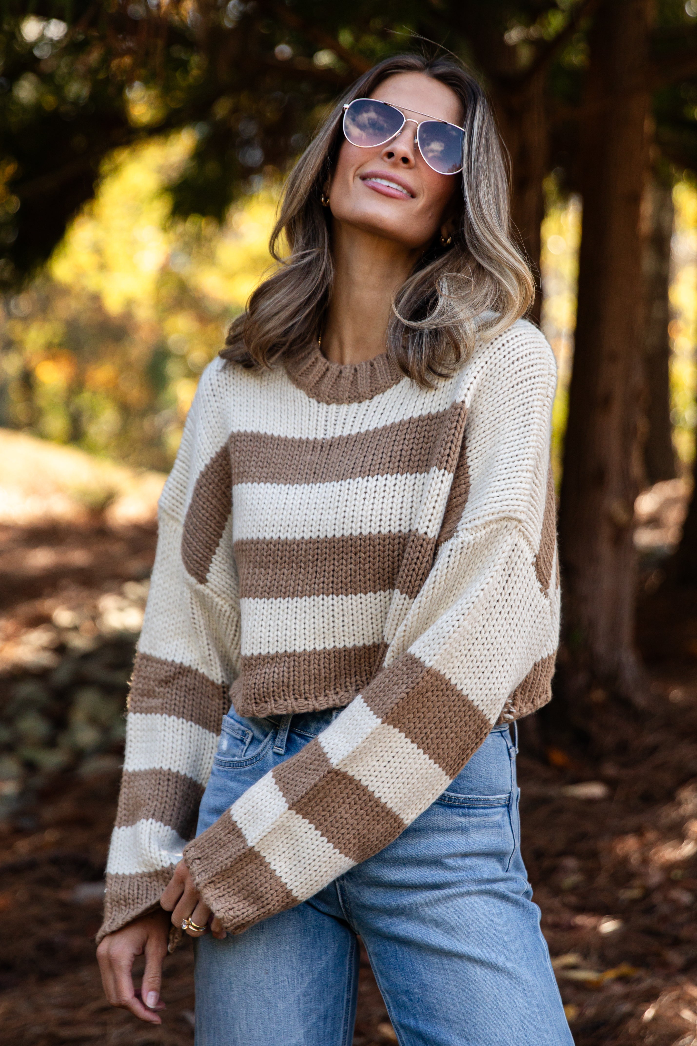 Woman wearing a striped sweater and sunglasses in a forest setting