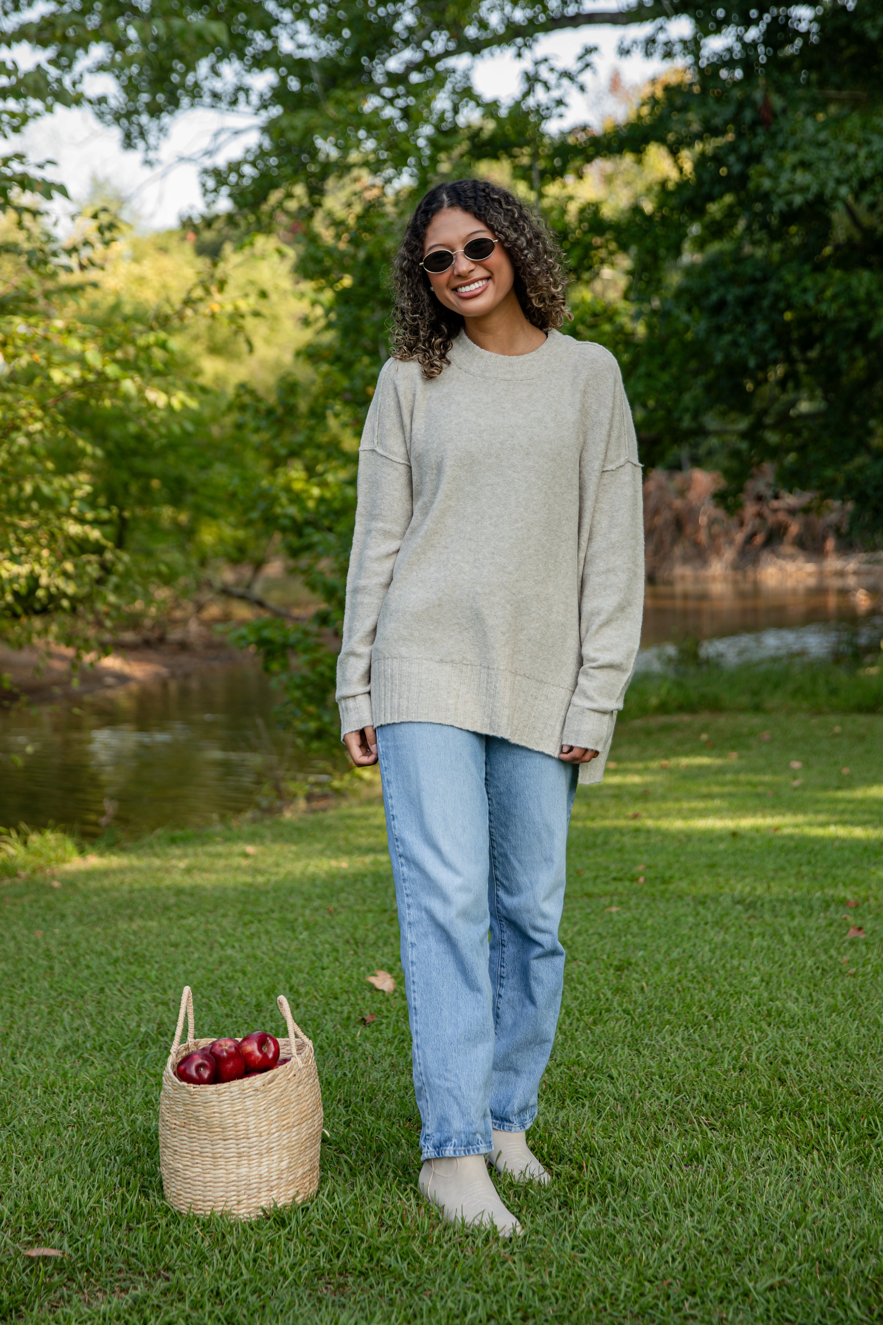Woman standing outdoors in a park with a basket of apples