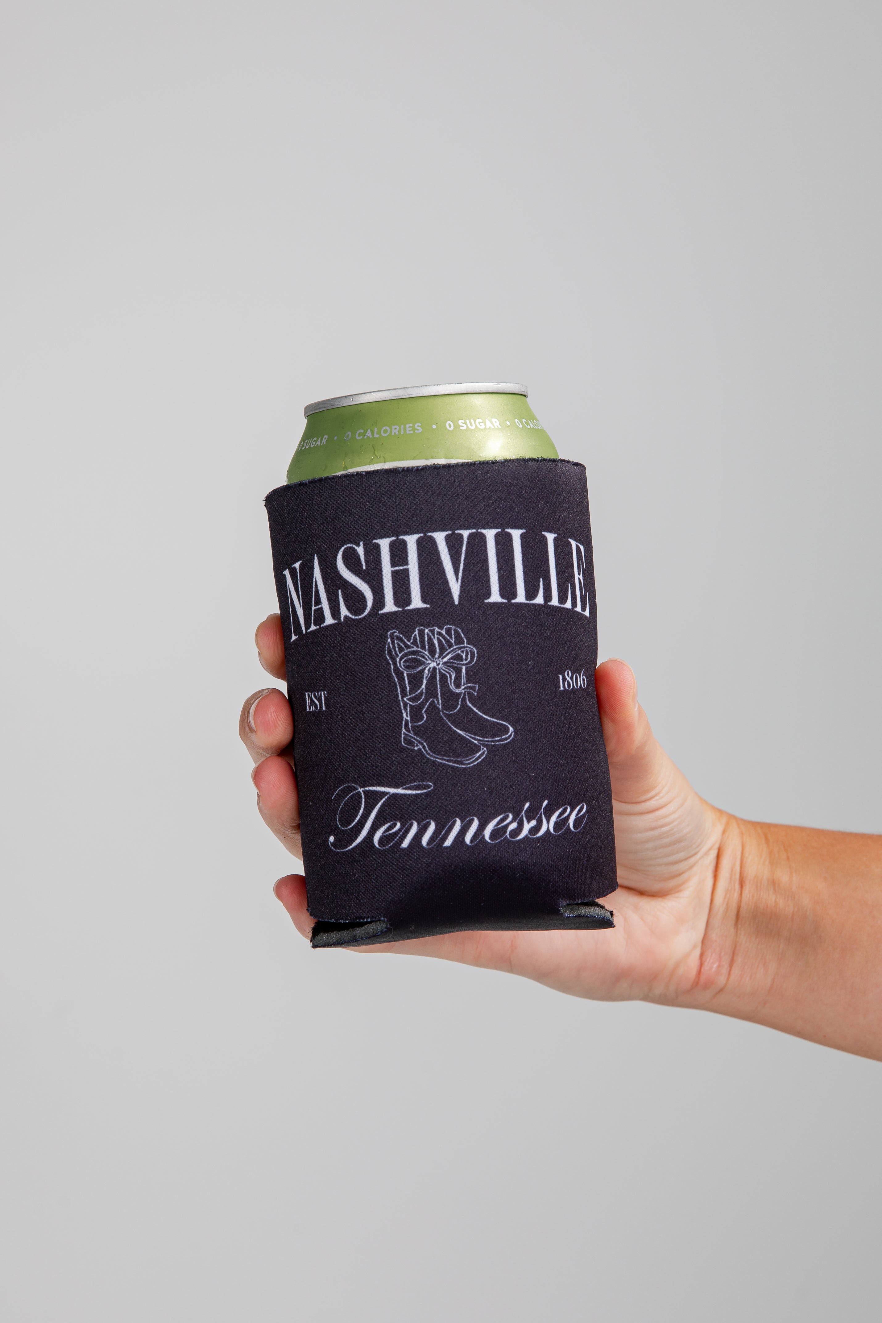Hand holding a can with a Nashville Tennessee koozie against a gray background