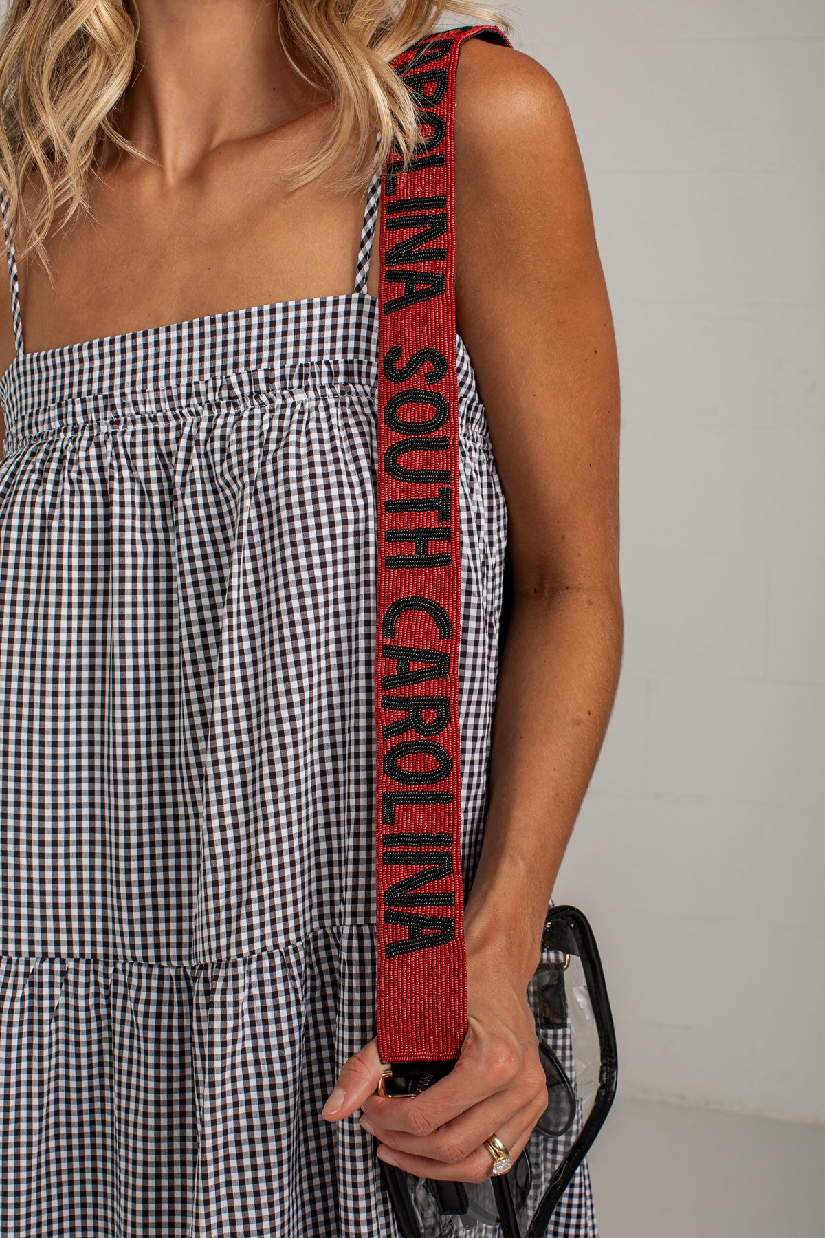 A close-up of a person wearing a black and white gingham dress, holding a red shoulder strap with &