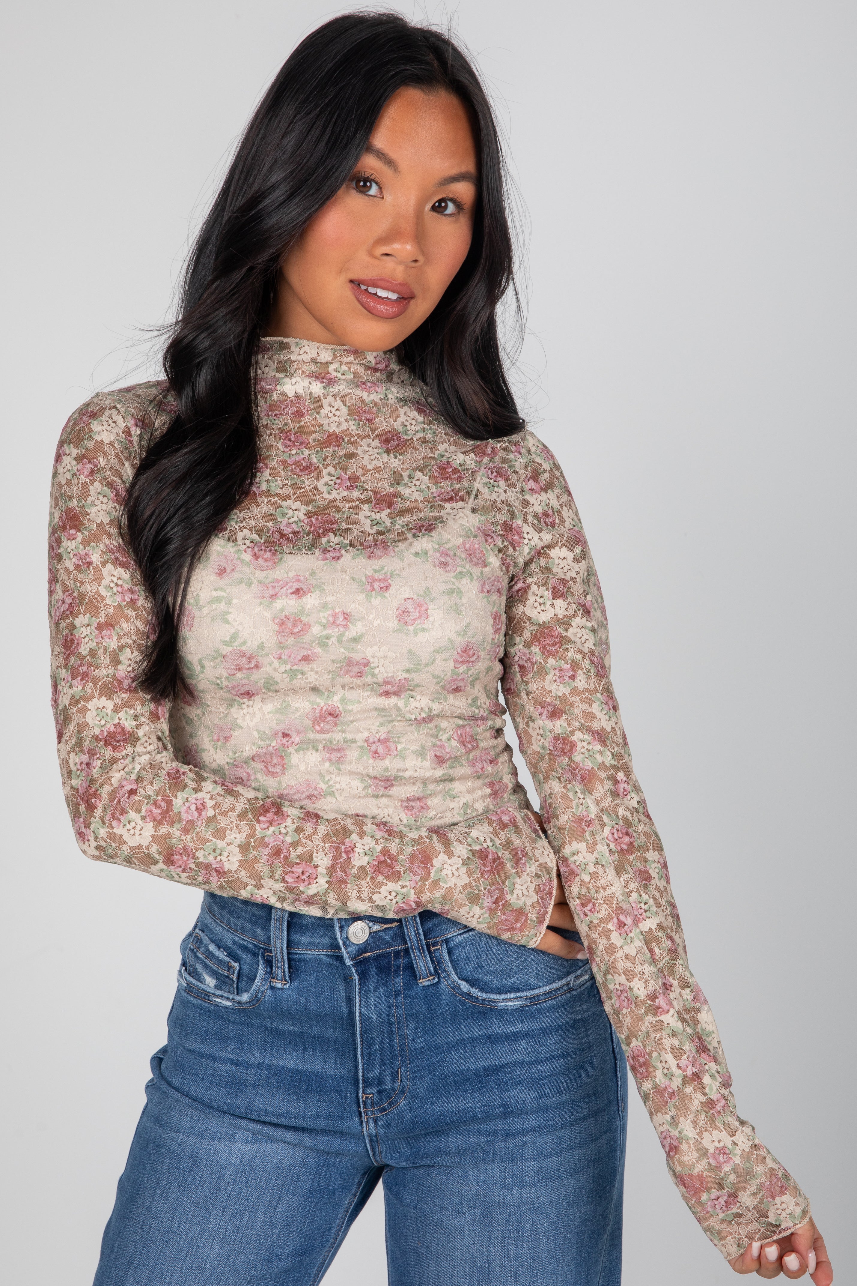 Woman wearing a floral long-sleeve top and blue jeans against a gray background