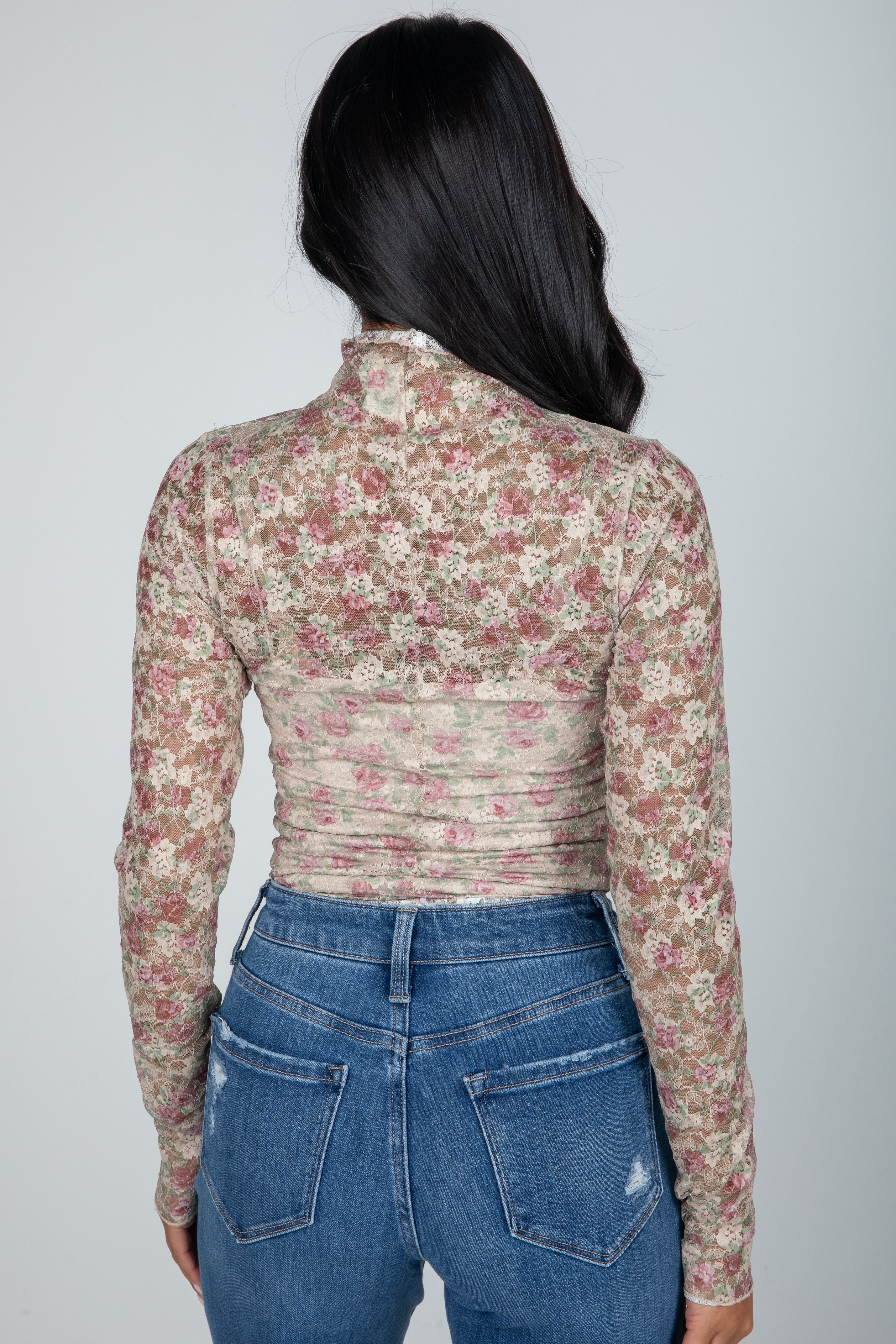 Person wearing a floral long-sleeve top and blue jeans on a plain background