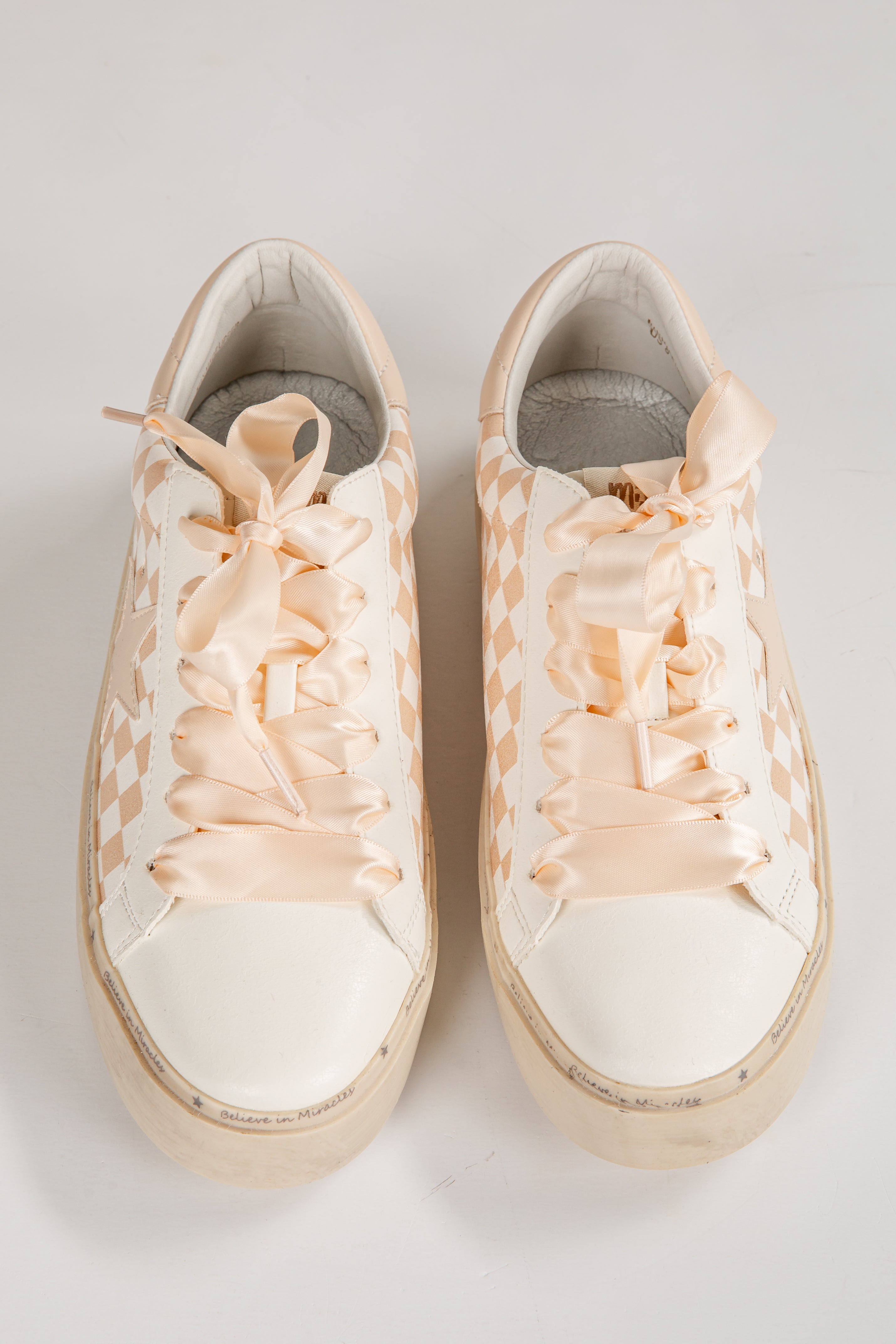 Pair of white sneakers with floral lace-up design on a light gray background