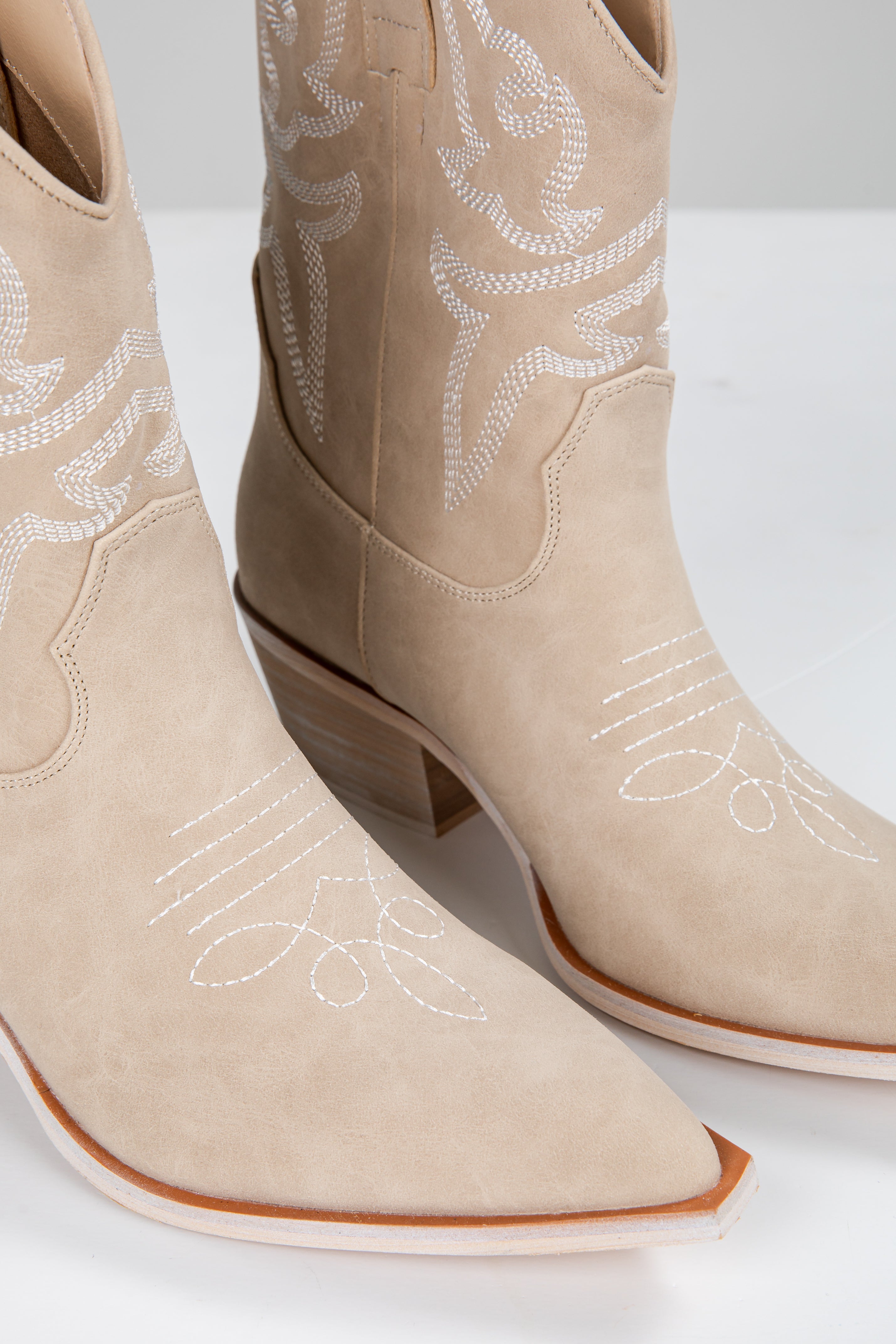 Beige cowboy boots with white embroidery on a white background