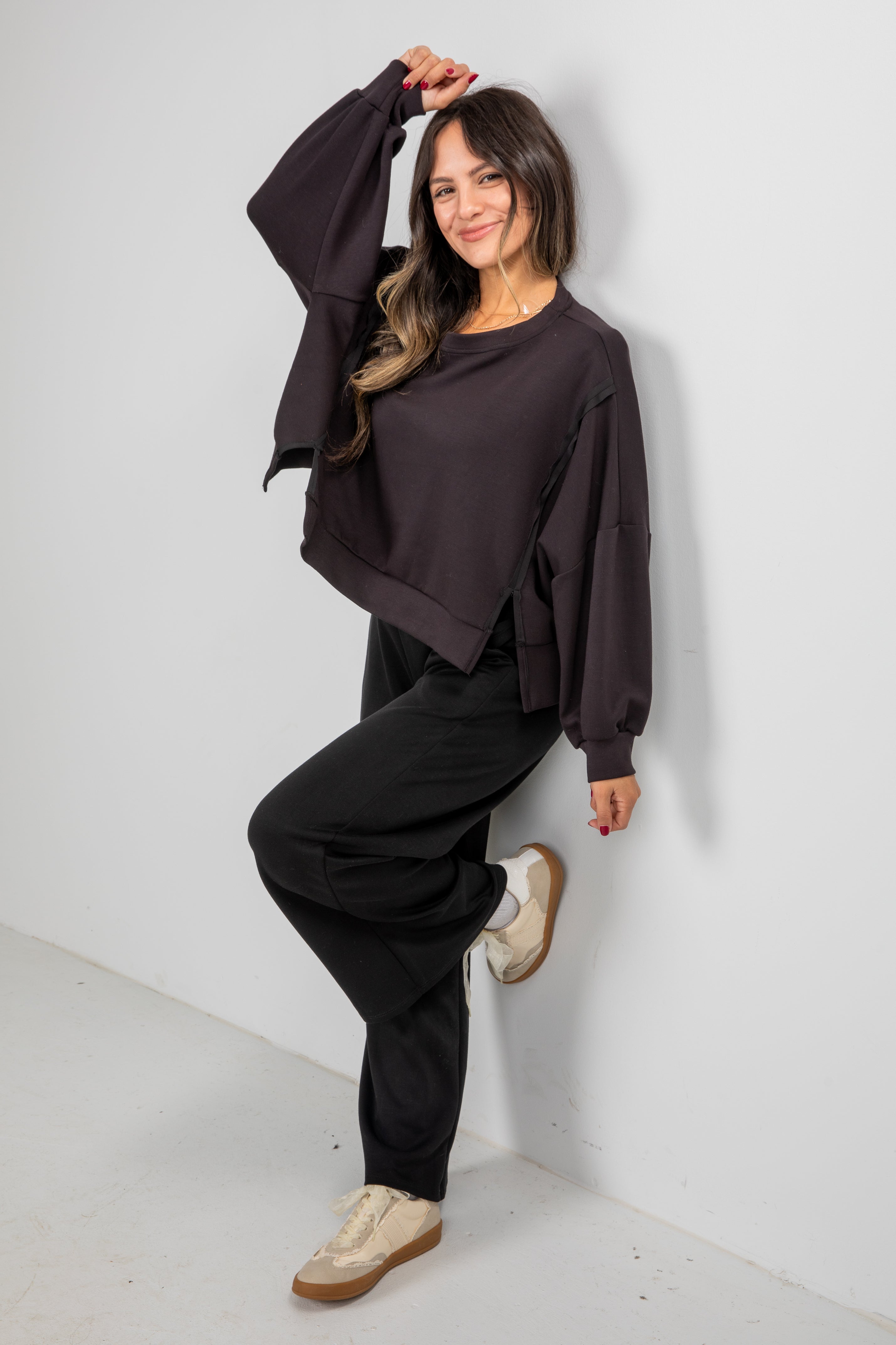 Woman wearing a dark brown oversized sweater and black pants against a white background